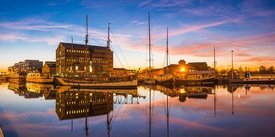 Sailing ships moored in Gloucester Docks beside Victorian warehouses at sunset