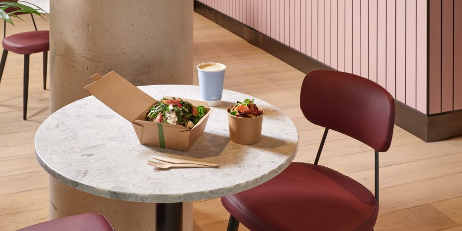 cafe area with pink interior, featuring a salad to go box and coffee takeaway cup on a table