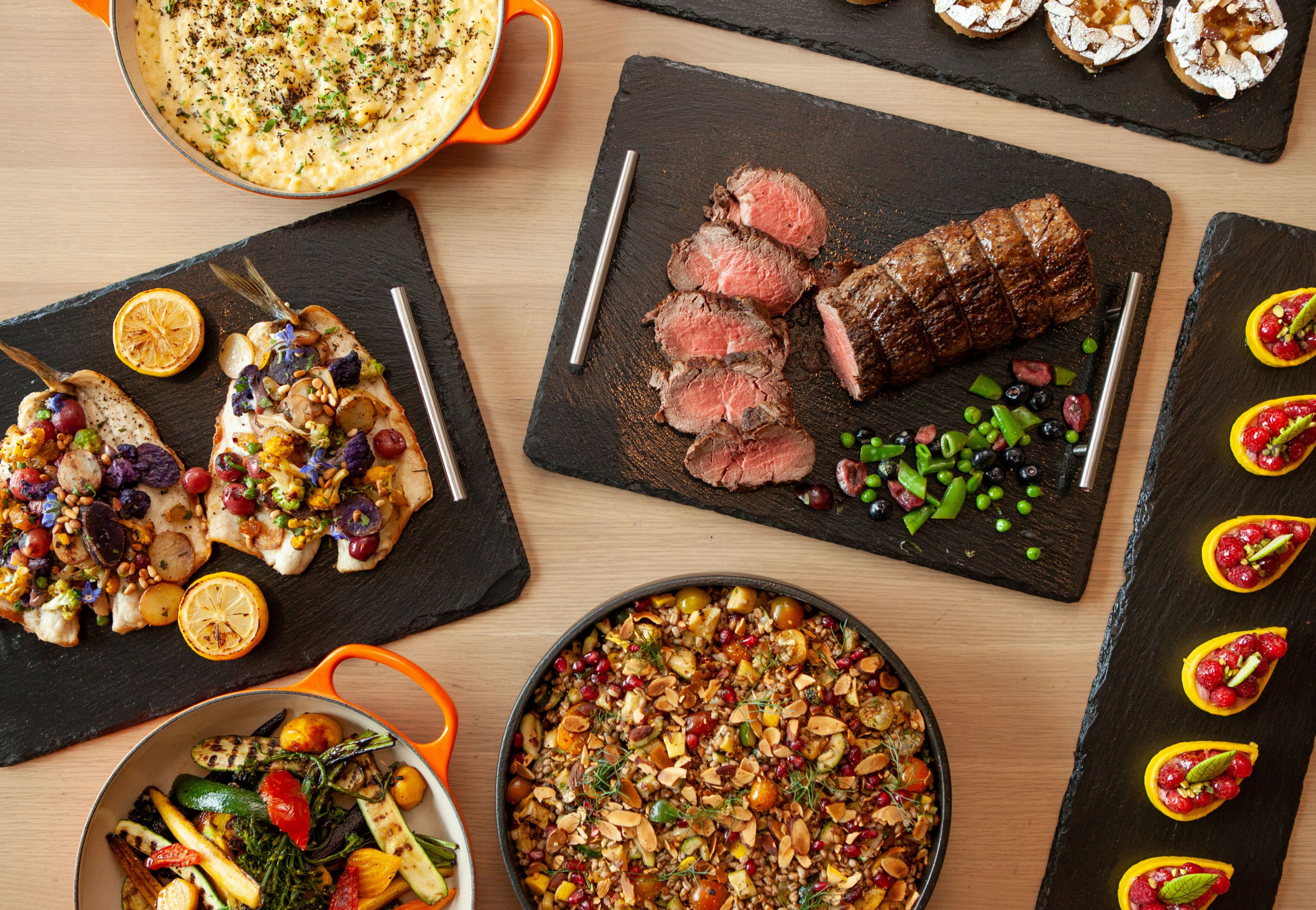 An assortment of gourmet dishes including sliced roast beef, stuffed vegetables, polenta, and colorful sides arranged on a table.