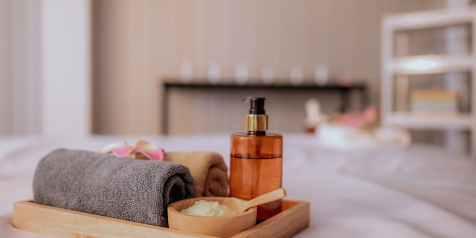 Bandeja de spa con toalla, botella de aceite y sales de baño cerca de la bañera