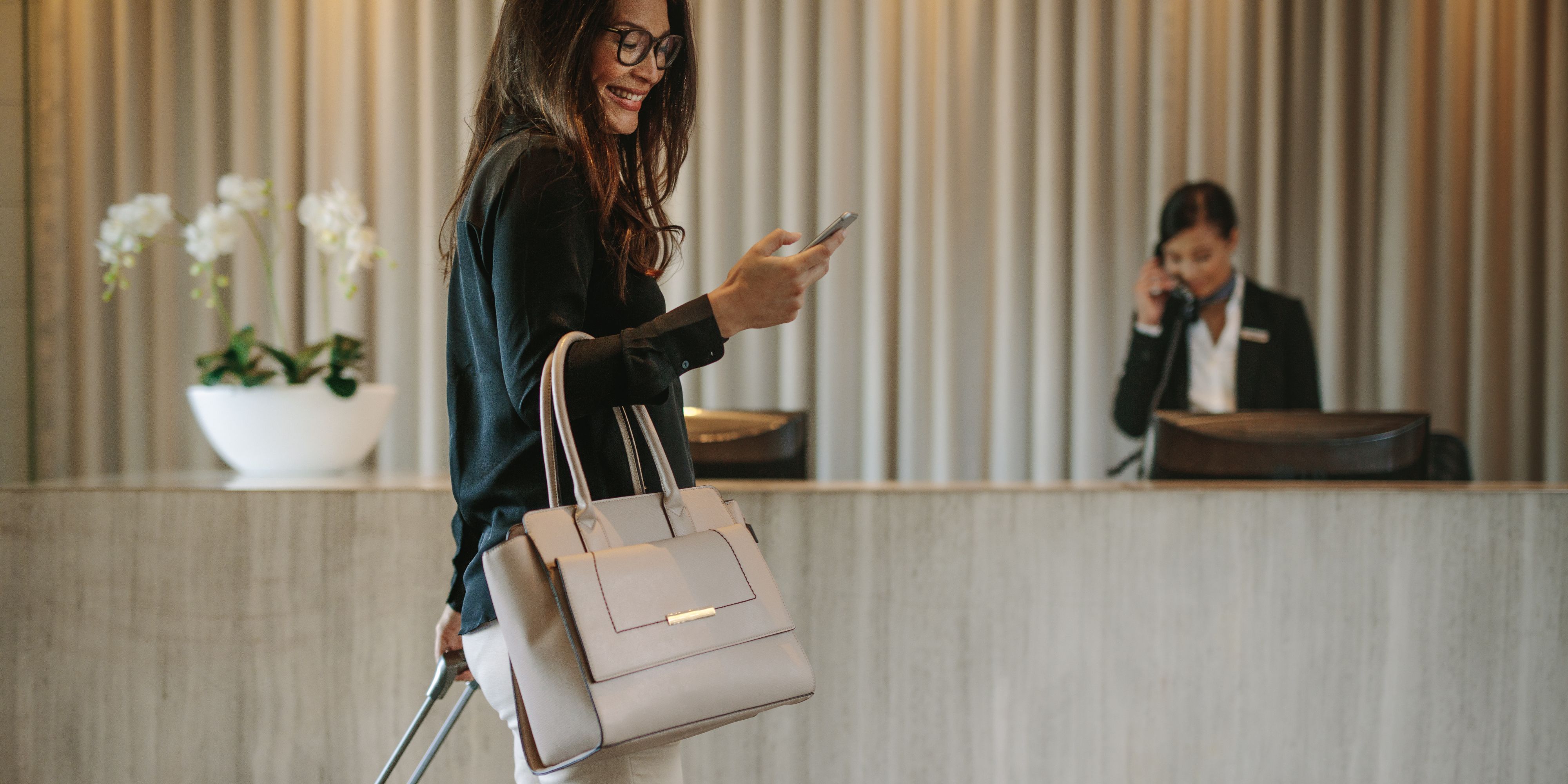 Guest arriving at the hotel, walking in the lobby while smiling at phone