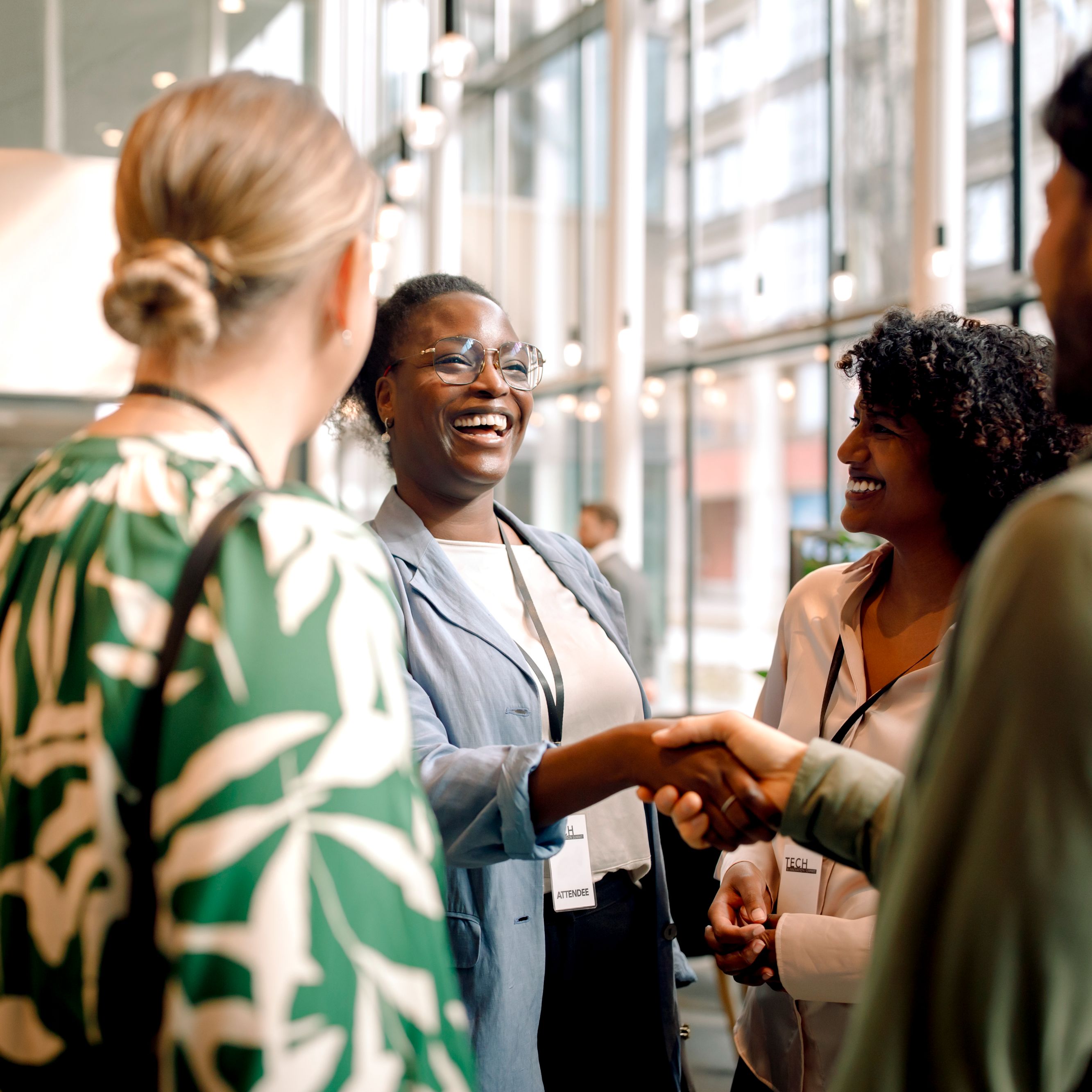 Conference attendees networking and shaking hands in a bright event space.