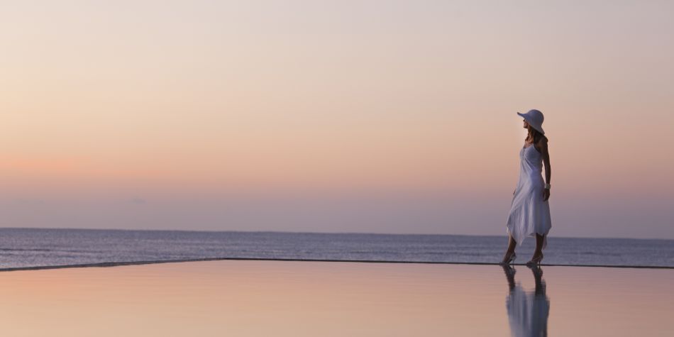 woman wearing white standing on the edge of the infinity pool overlooking the ocean at sunset