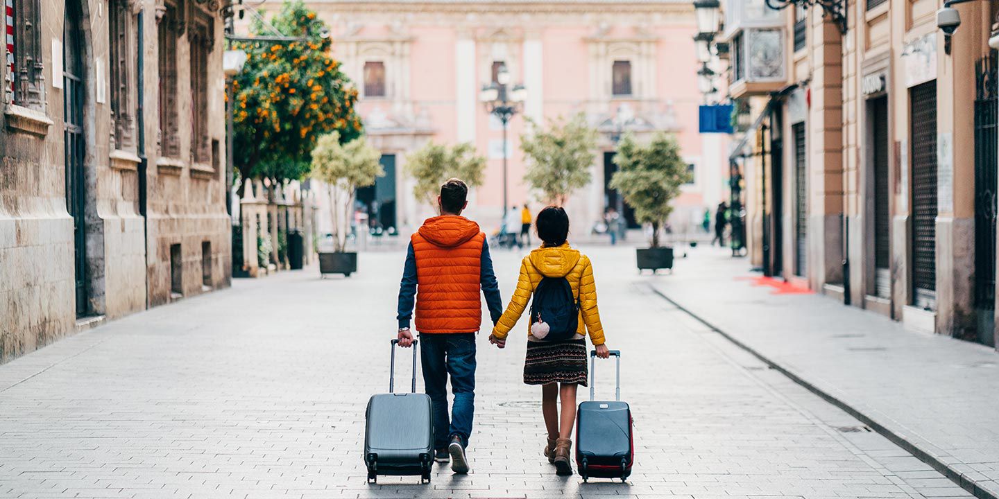 Un couple marche dans la rue en se tenant la main et en tirant leurs valises