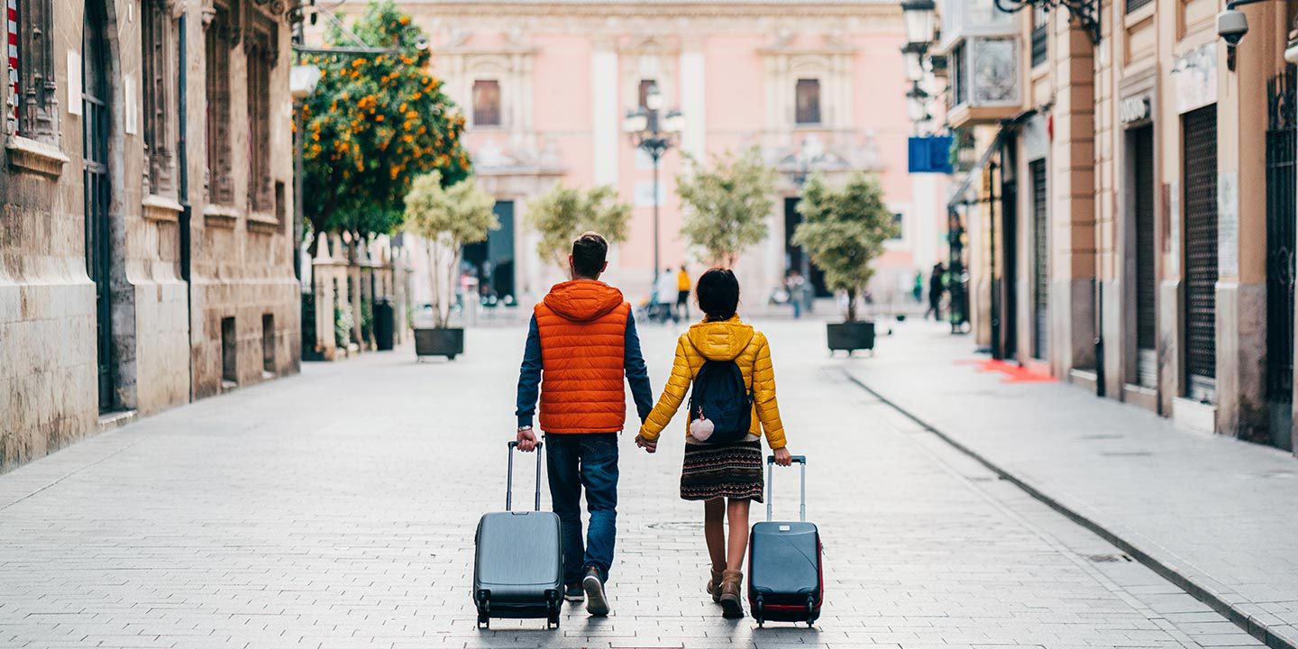 Couple walking down the street hand in hand with their suitcases