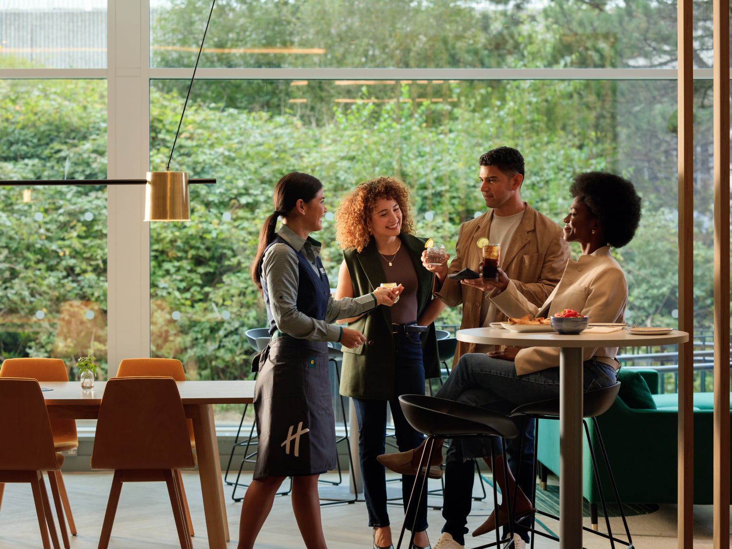 Guests standing together near a high-top table in a bright hotel event space with floor-to-ceiling windows.