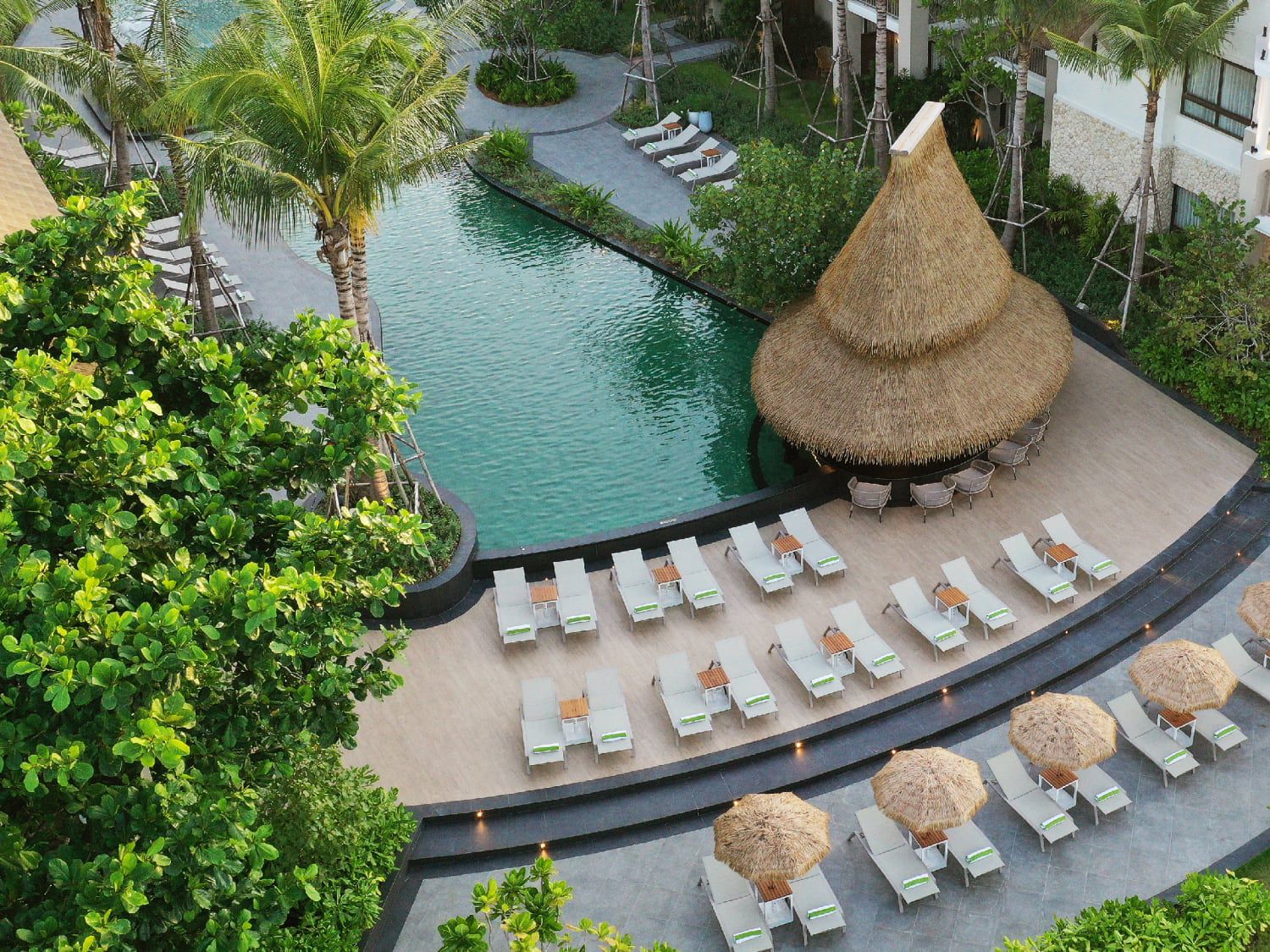 Aerial shot of resort pool with grass hut and ample comfortable seating