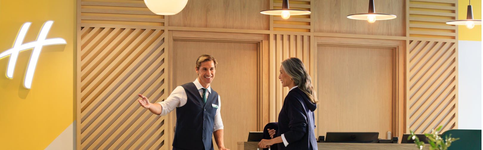 Hotel staff member greeting a guest in a modern lobby with warm wood accents and yellow wall decor.