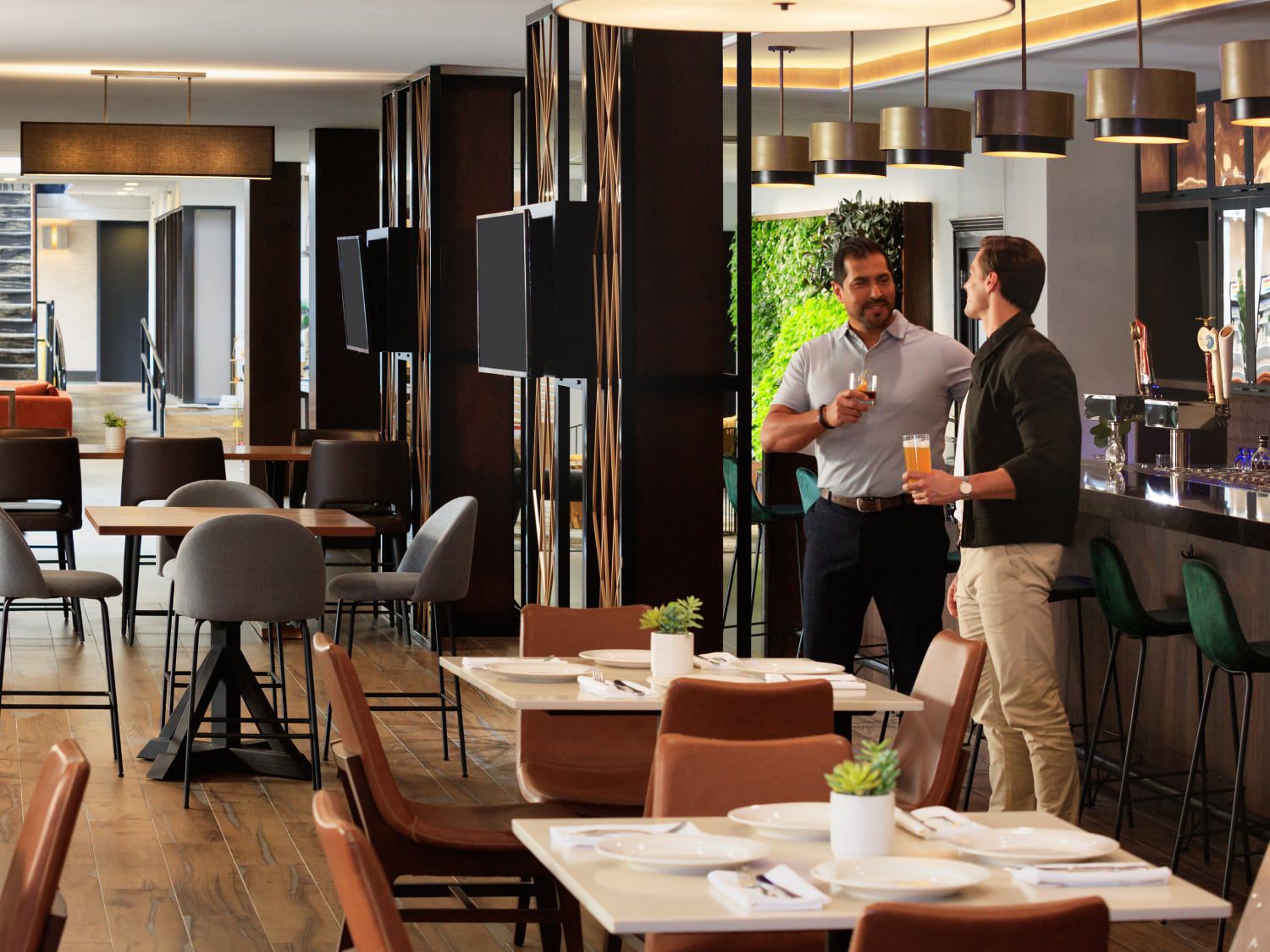 Der Restaurant- und Barbereich des Hotels mit gedeckten Tischen, Sitzplätzen an der Theke und Personal in der Nähe der offenen Küche.