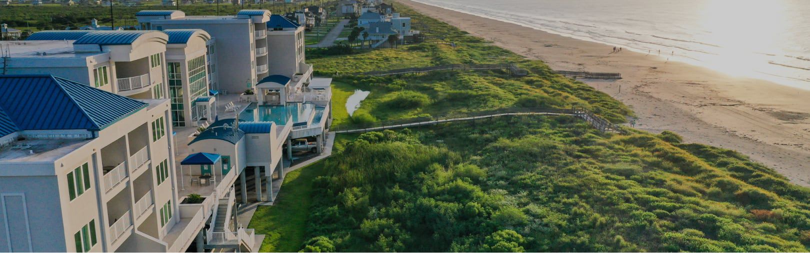An oceanfront resort facing lush dunes and a low tide beach at sunrise.