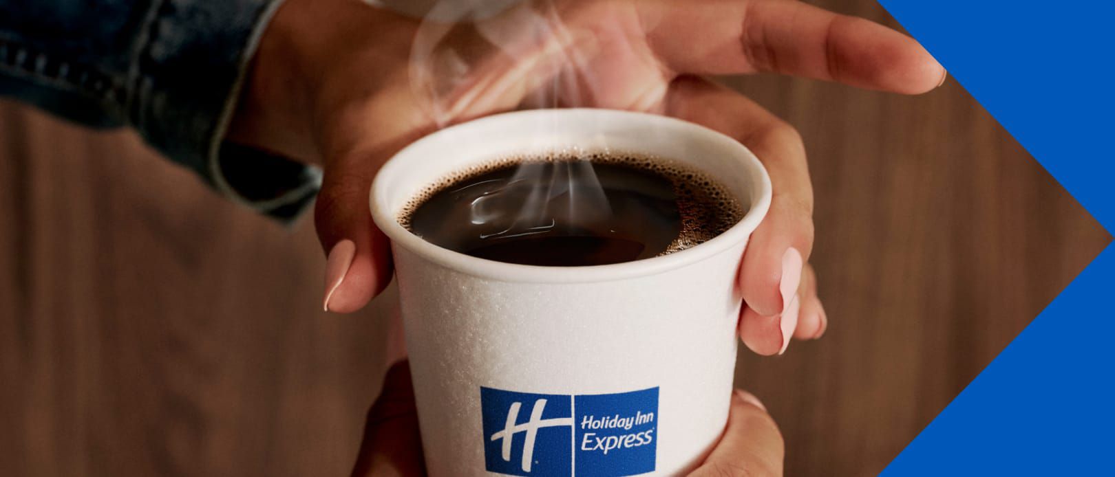 Hands hold a steaming cup of coffee with the Holiday Inn Express logo.