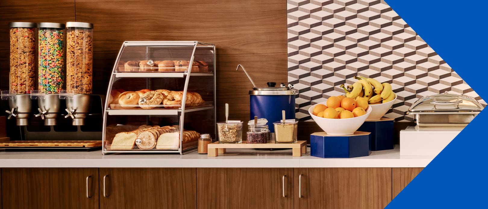 A hotel breakfast bar displays cereal, pastries, yogurt, and fresh fruit.