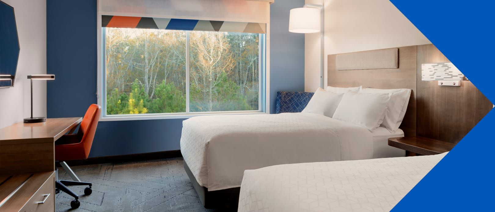 A bright Holiday Inn Express guest room with two beds, a desk, and a large window overlooking greenery.