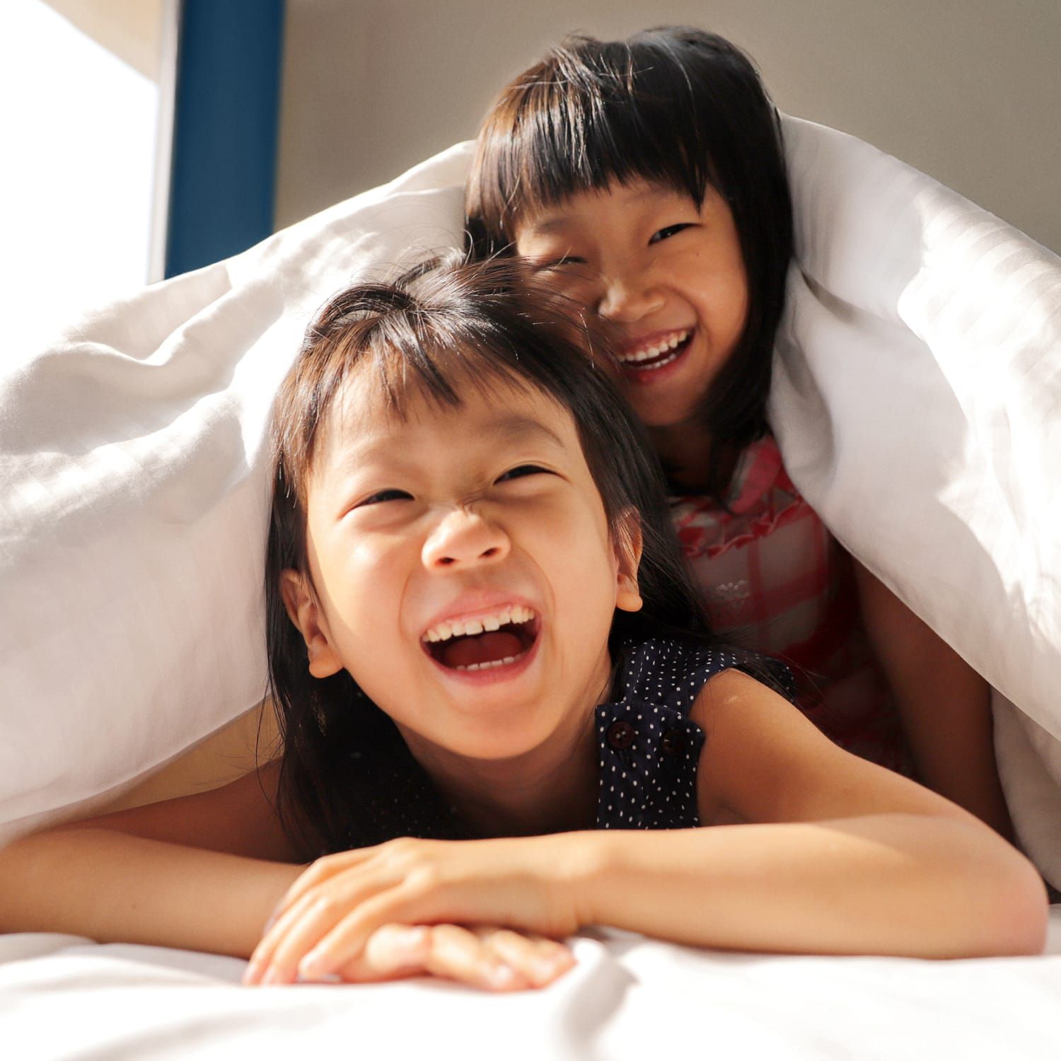 Two girls giggling in a comfortable bed under a plush duvet.