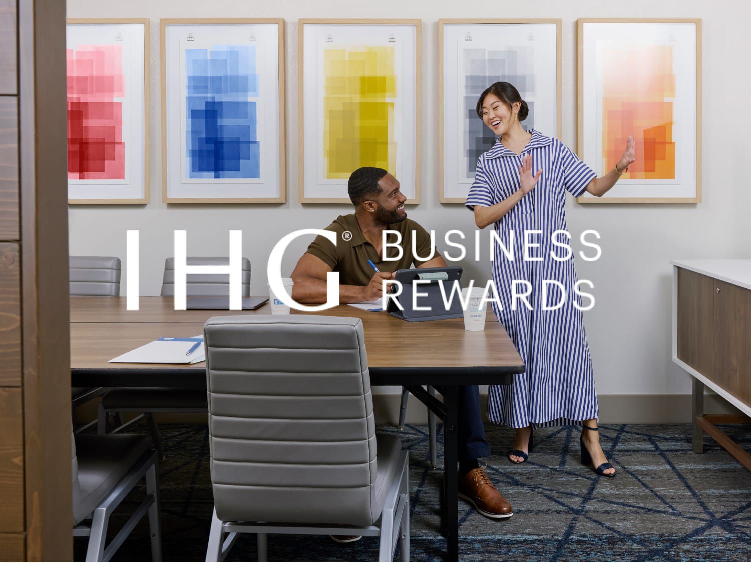 A man and woman in a conference room preparing for a presentation with the IHG Business Rewards logo overlaid.