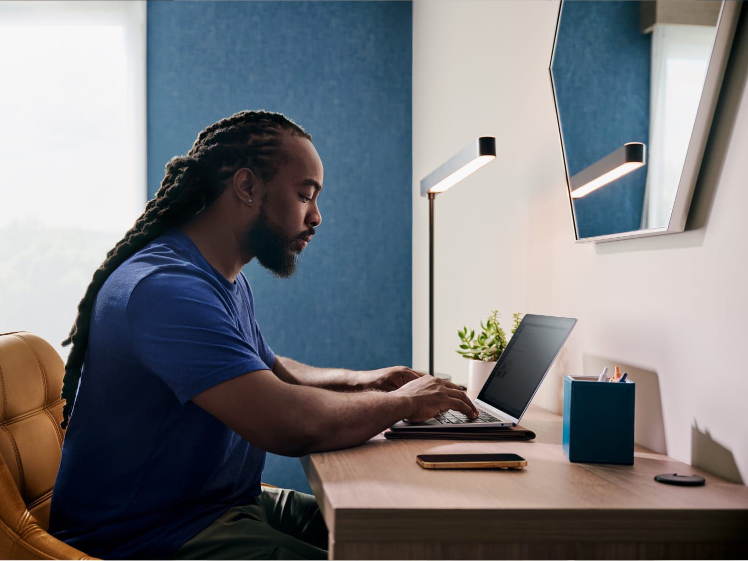 Un hombre trabaja con una computadora portátil en un escritorio dentro de una habitación de hotel bien iluminada.