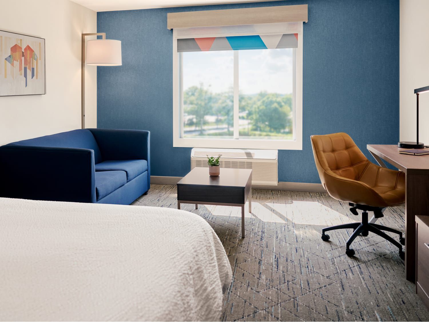Una habitación del Holiday Inn Express con cama, sofá, escritorio y un gran ventanal.
