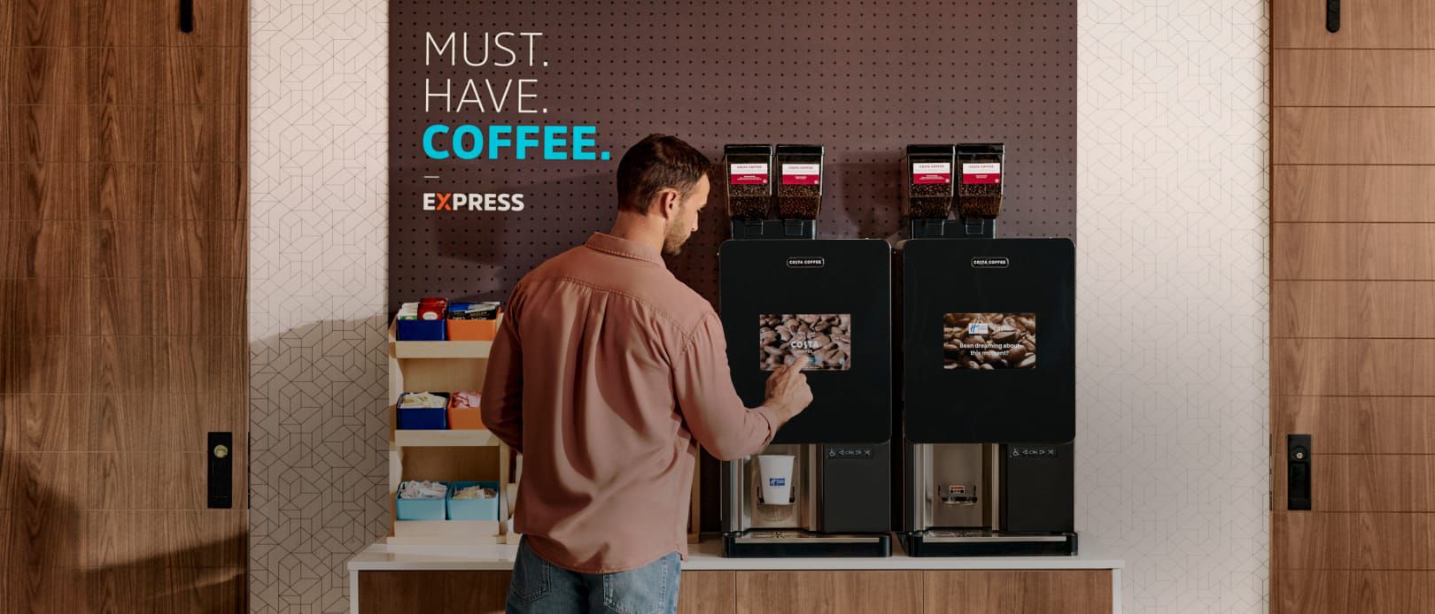 Man using coffee machine at Holiday Inn Express with “Must. Have. Coffee.” sign