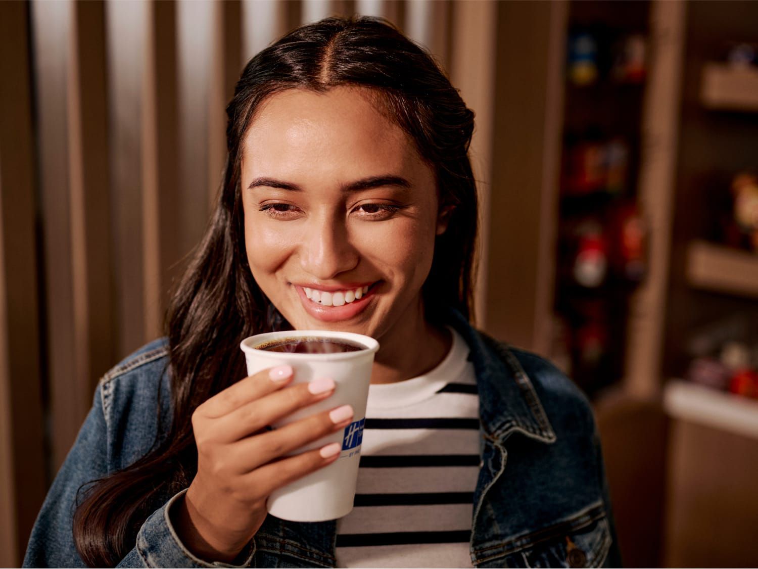 Smiling woman in denim jacket holding a Holiday Inn Express coffee cup