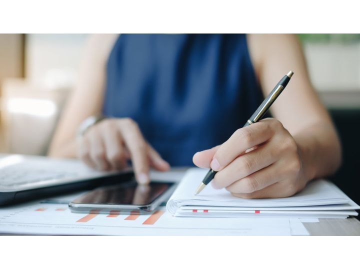 Menulis di atas kertas sambil menggulir layar pada ponsel dengan tangan yang lain