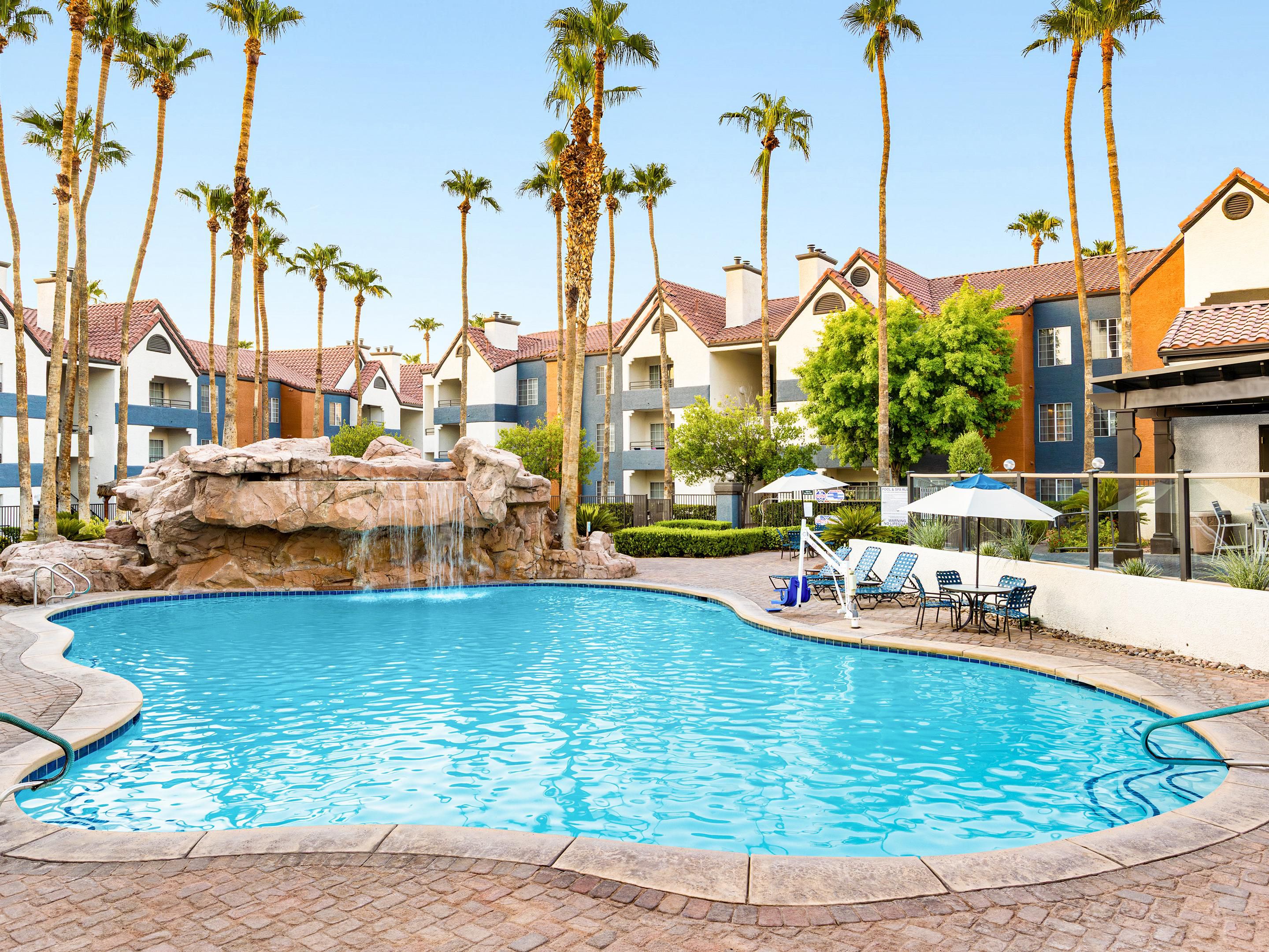 Resort pool with waterfall feature and surrounding palm trees.