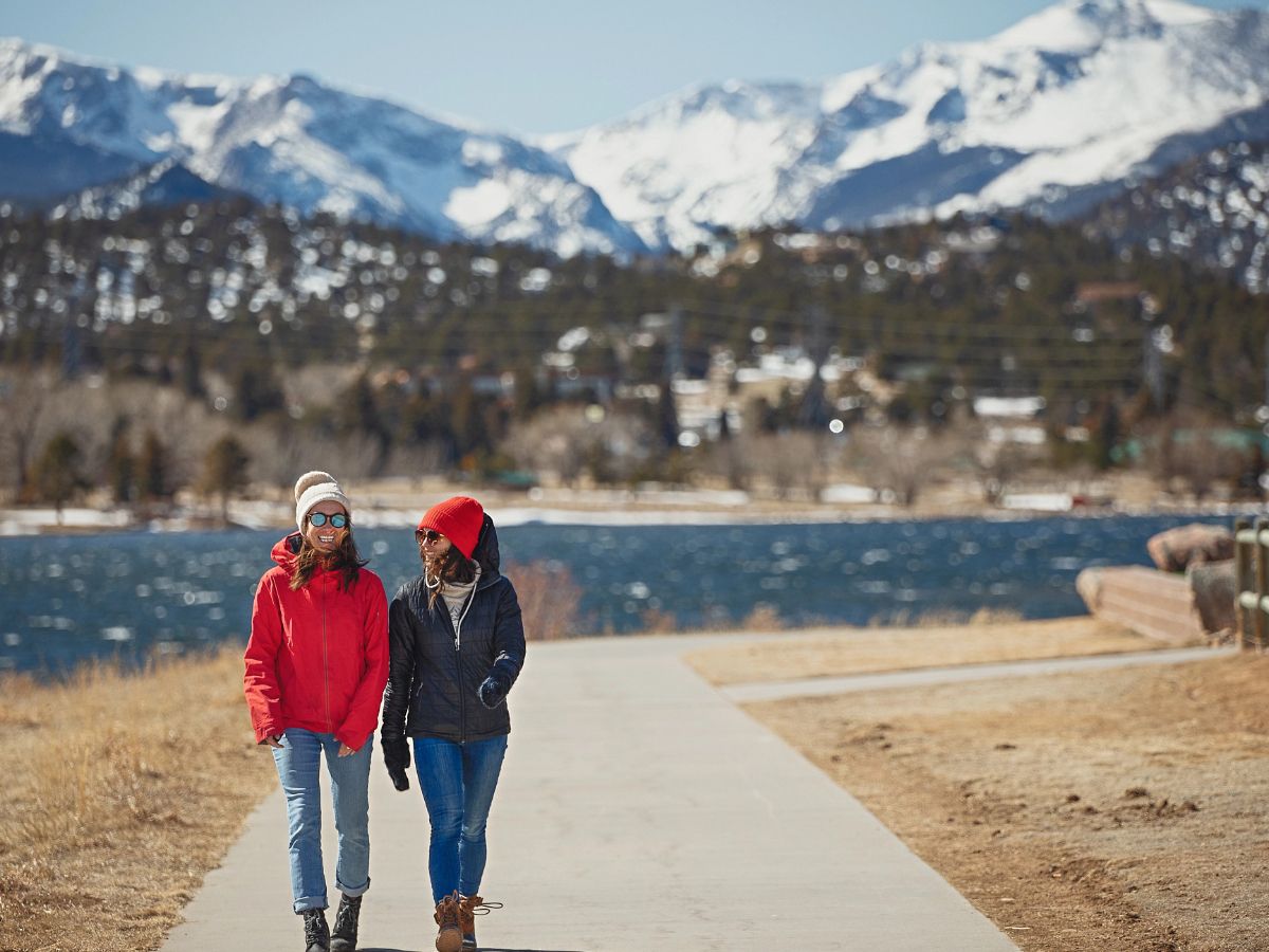 Two women walking on a paved trail at the foot of the Rocky Mountains