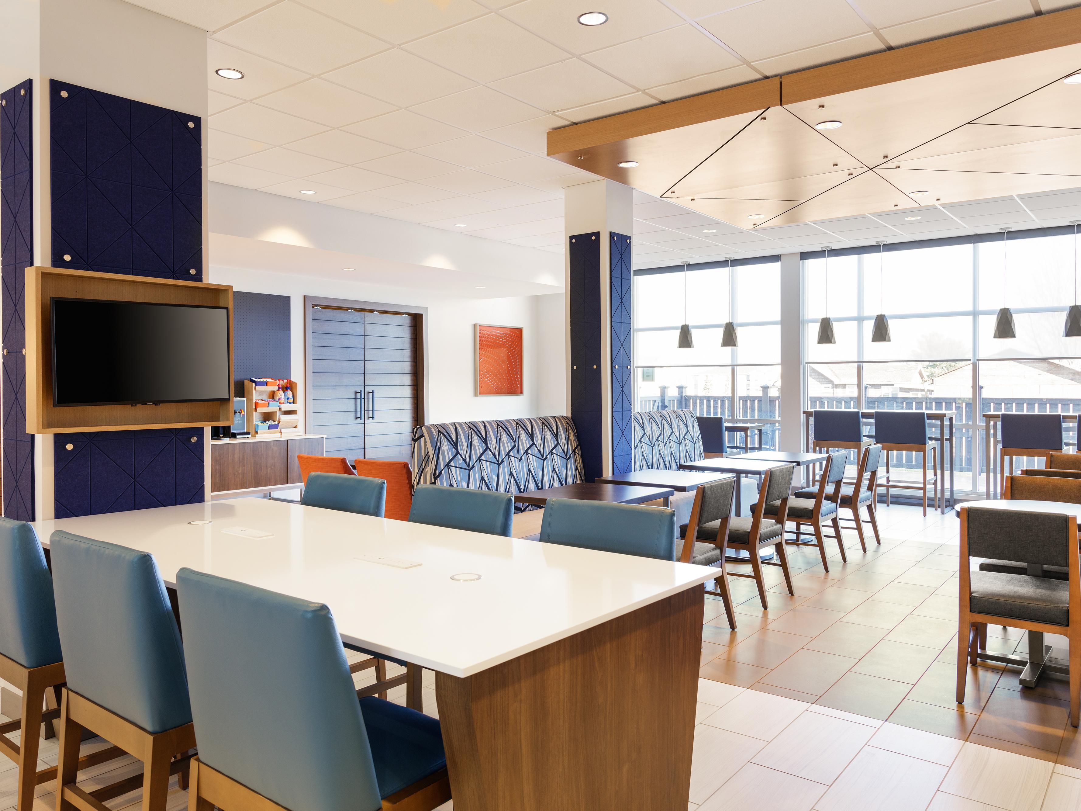 Bright modern hotel lobby with blue chairs and a TV screen.