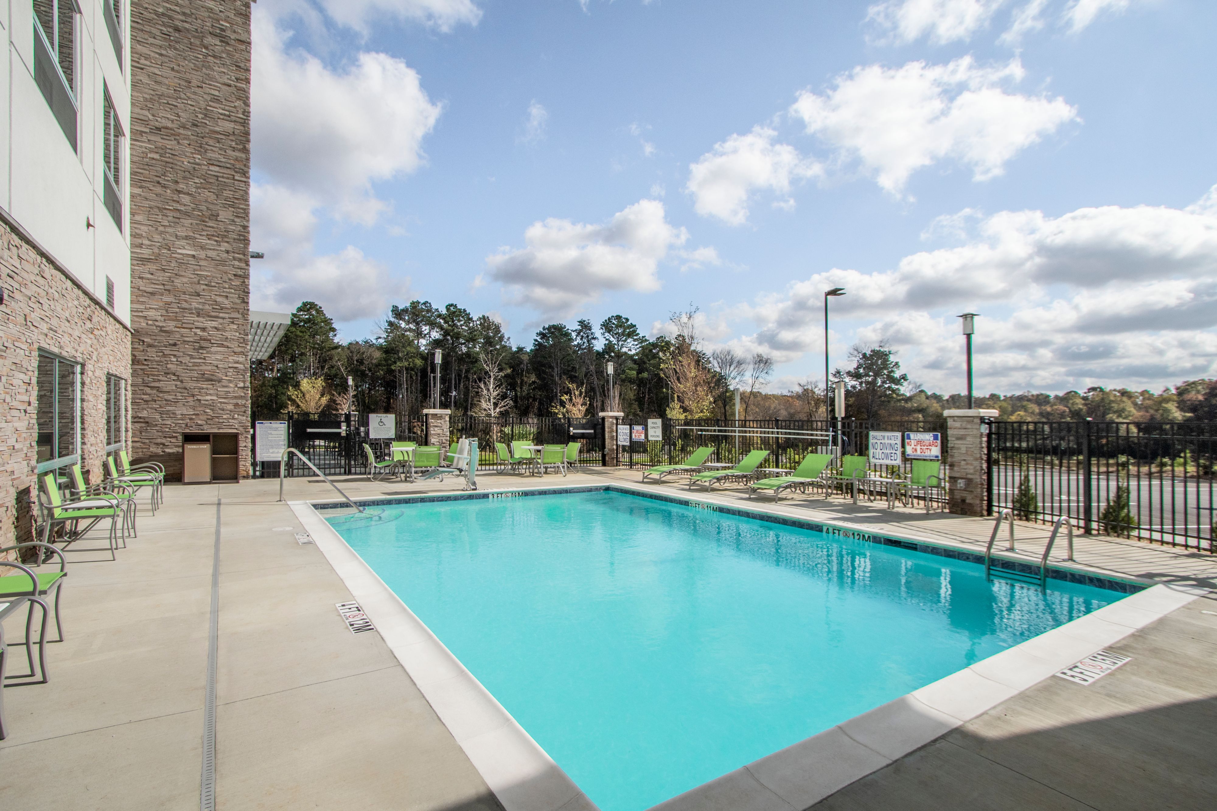 Seasonal outdoor swimming pool at Holiday Inn Express Charlotte Southwest with lounge chairs and surrounding trees