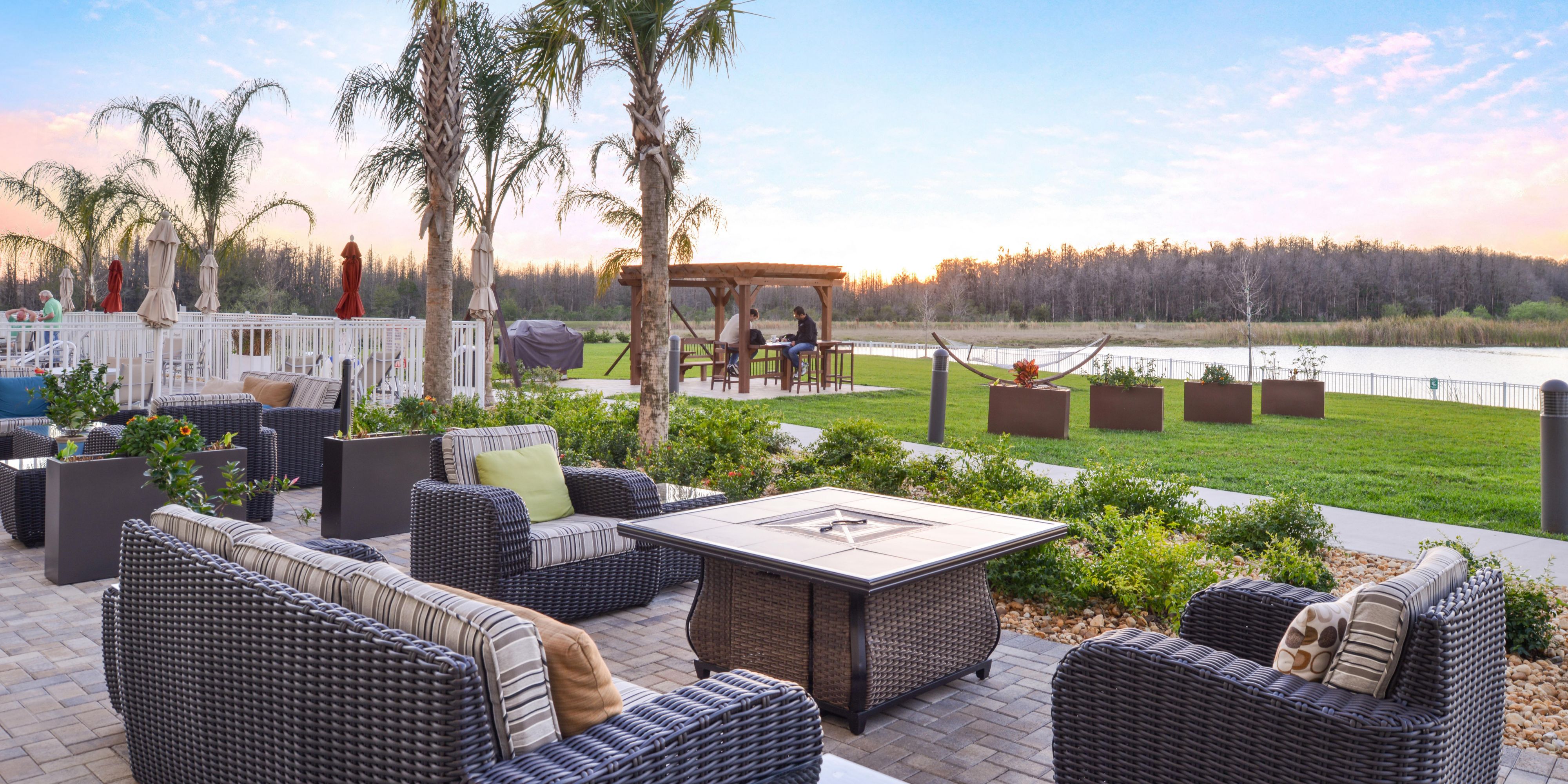 Guests enjoy a heated outdoor pool and hot tub set next to a tropical sundeck with fire pit,  grill, hammocks, and corn hole.