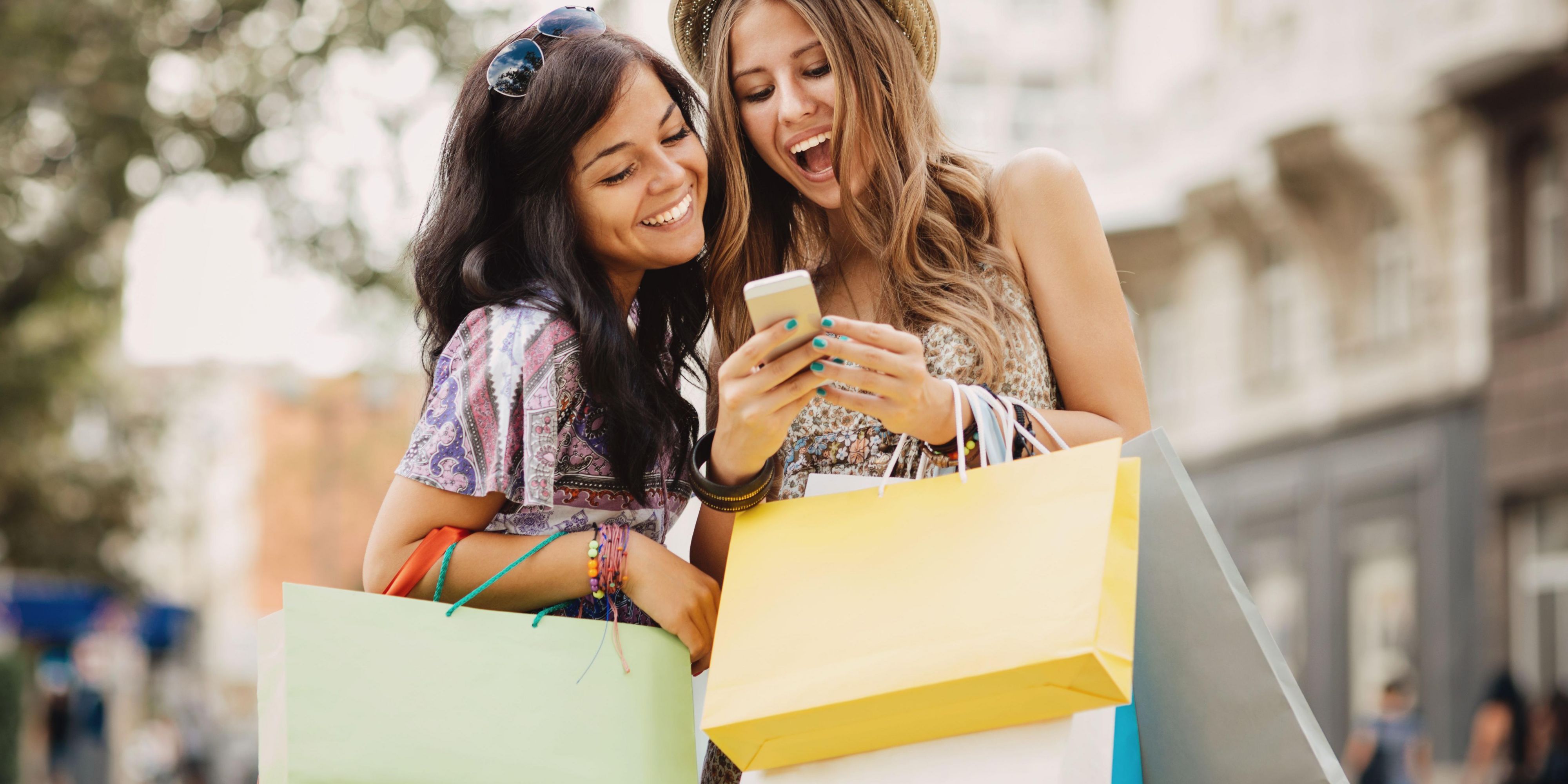 Friends shopping and smiling at phone with bags