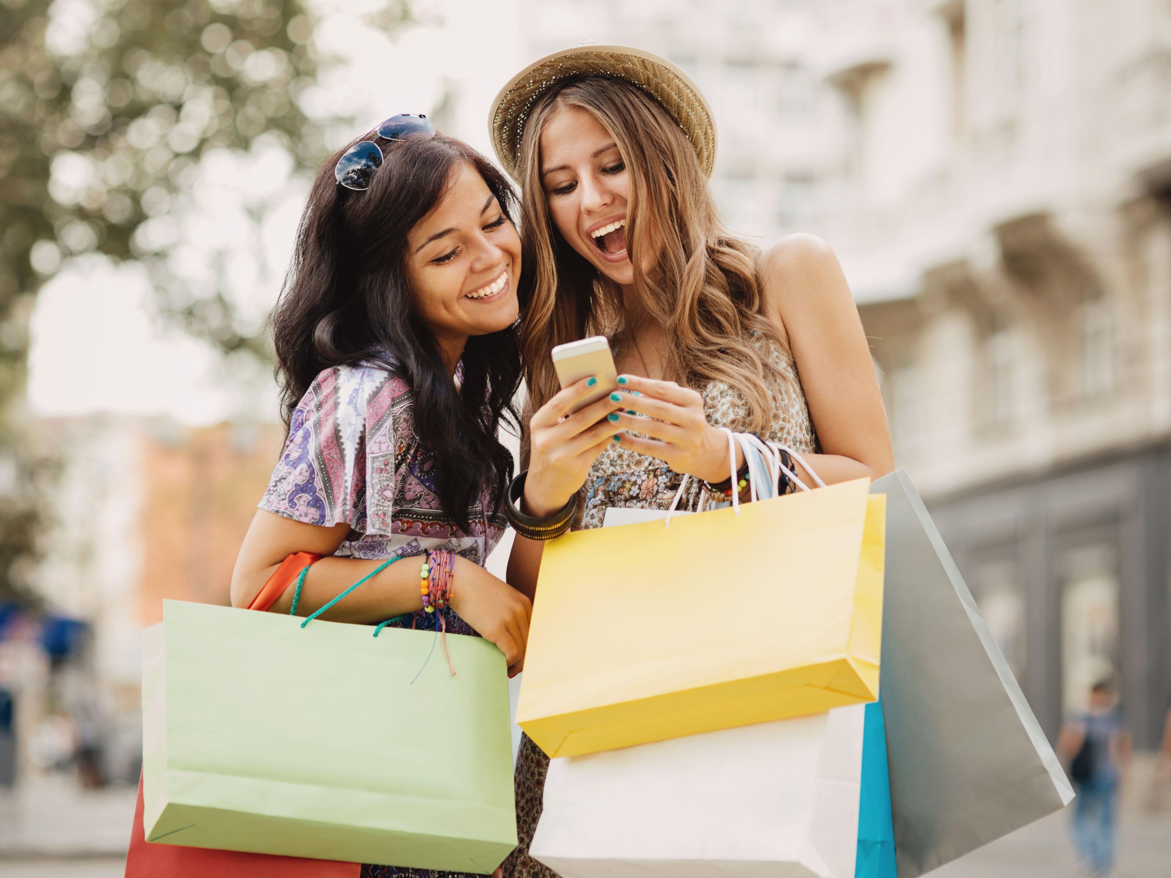 Friends shopping and smiling at phone with bags
