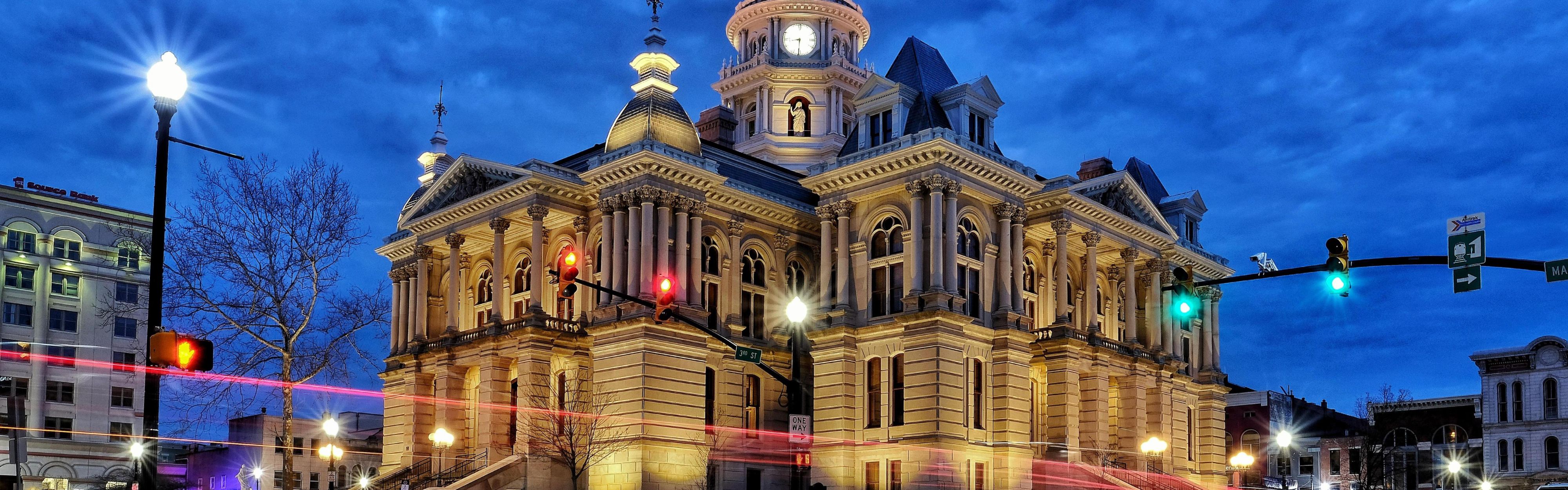 Lit historic courthouse at dusk with an electric board nearby