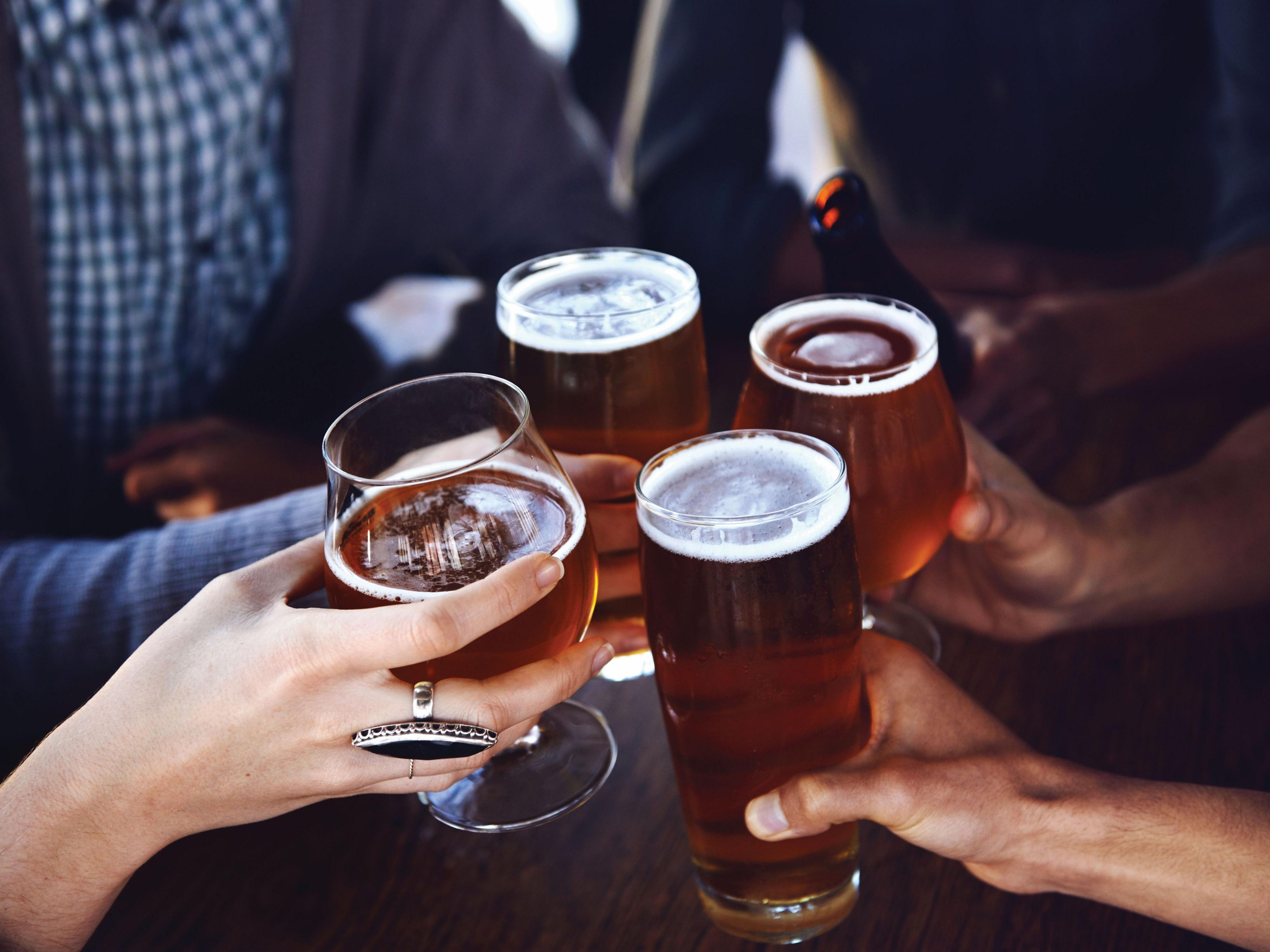 Friends toast with glasses of beer around a table.