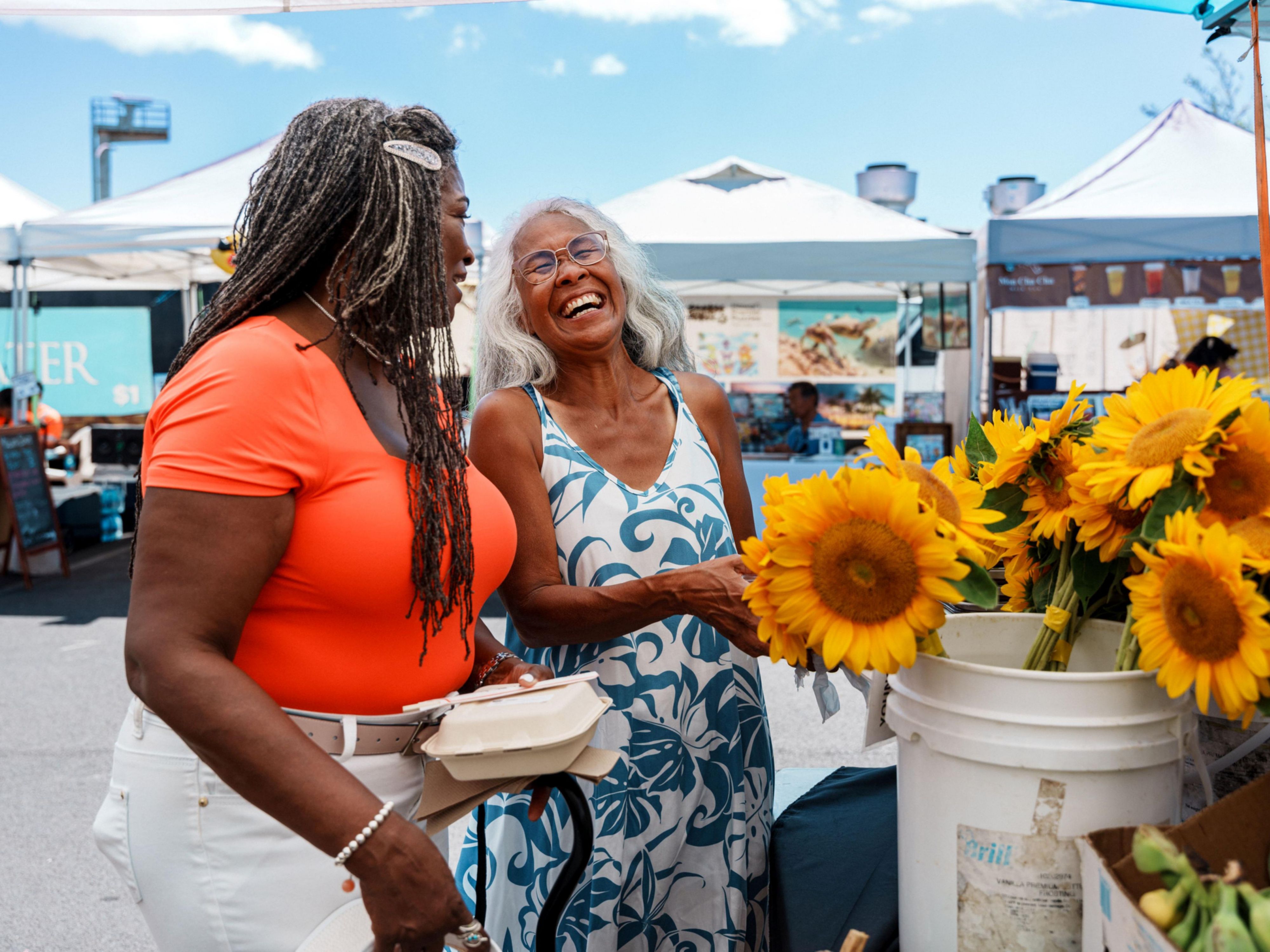 Two people chat beside bright sunflowers at an outdoor market.