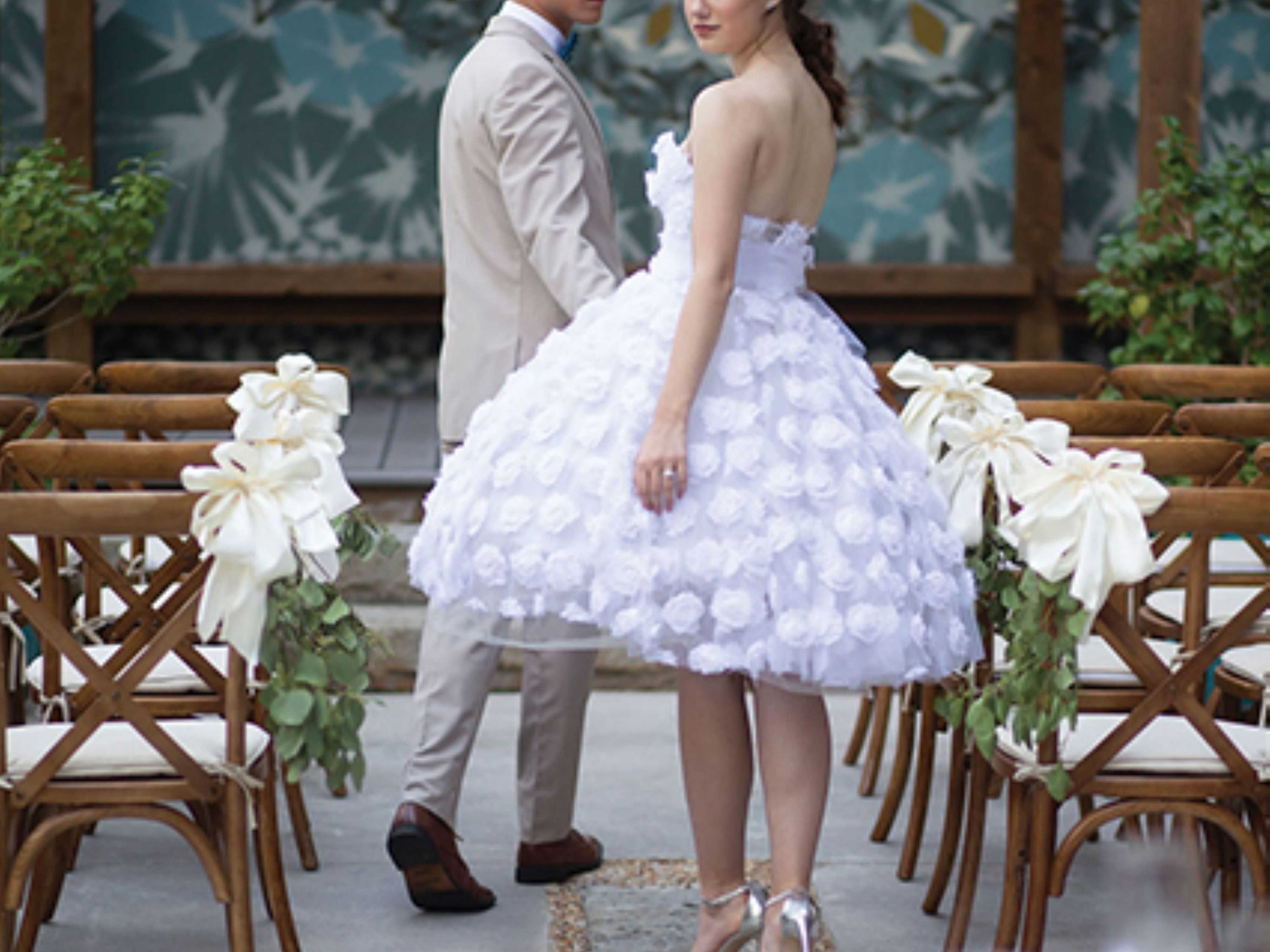 A couple walks down an outdoor aisle lined with decorated chairs.