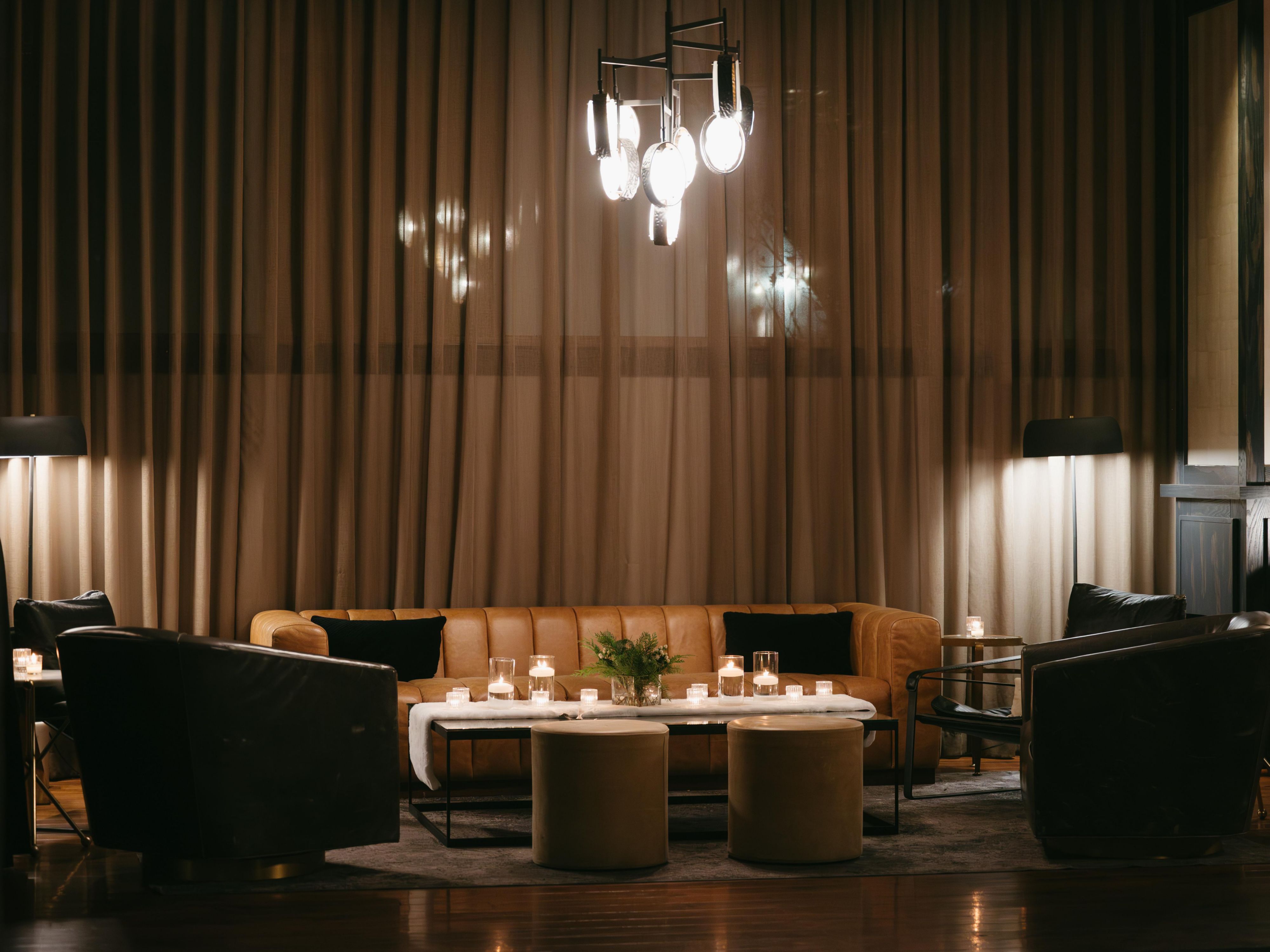 Stylish lounge with leather sofa, drapery, and chandelier.