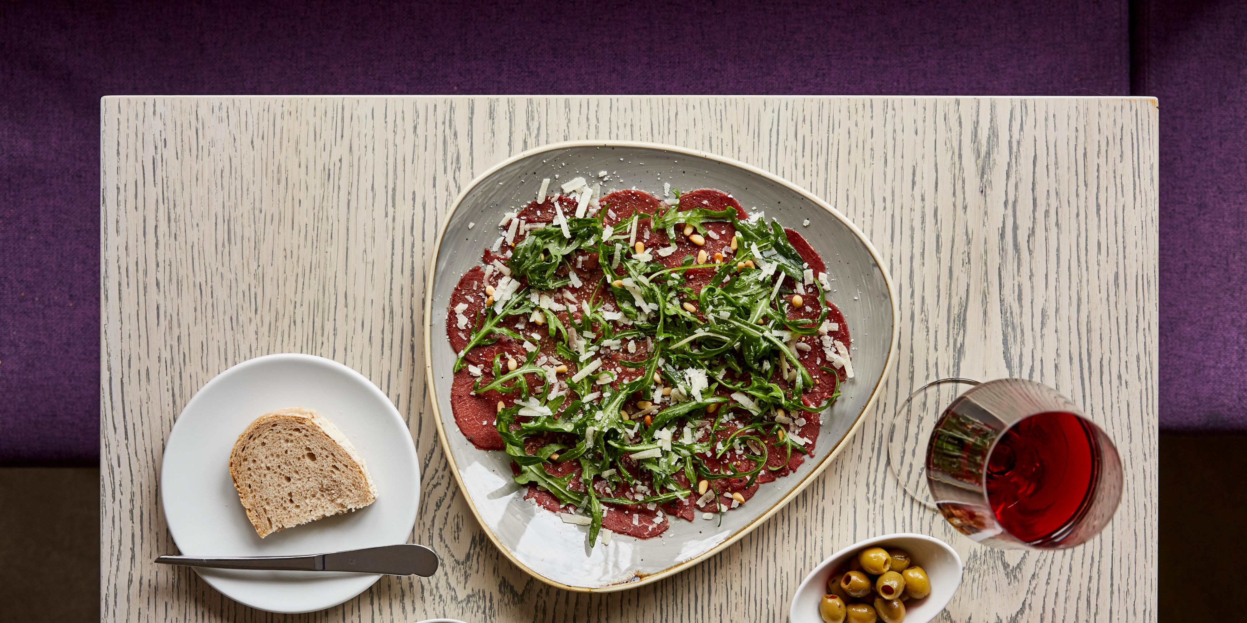 A tasty dish of beef carpaccio, with a glass of red wine. 