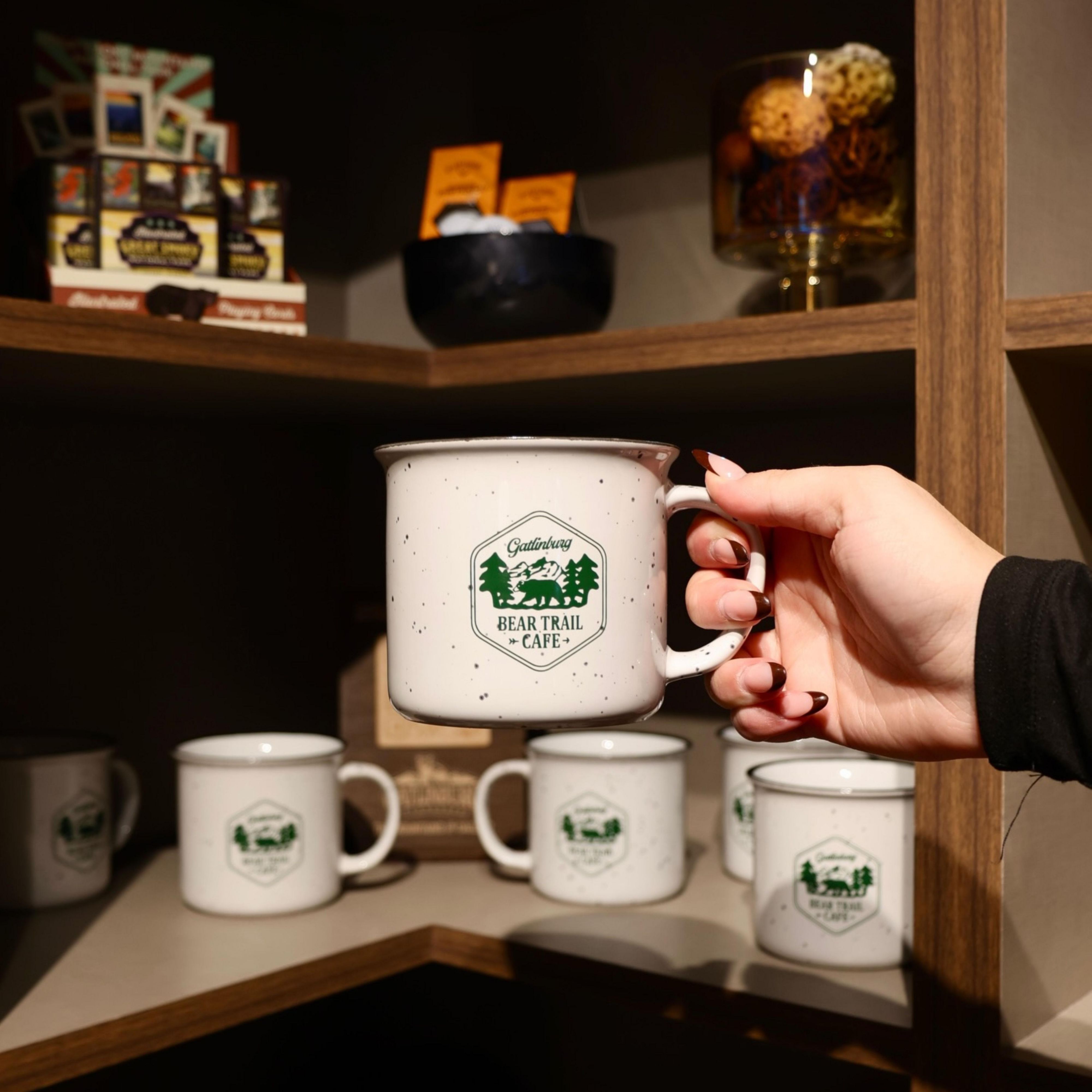 Guest holding a branded mug beside a display of coffee cups