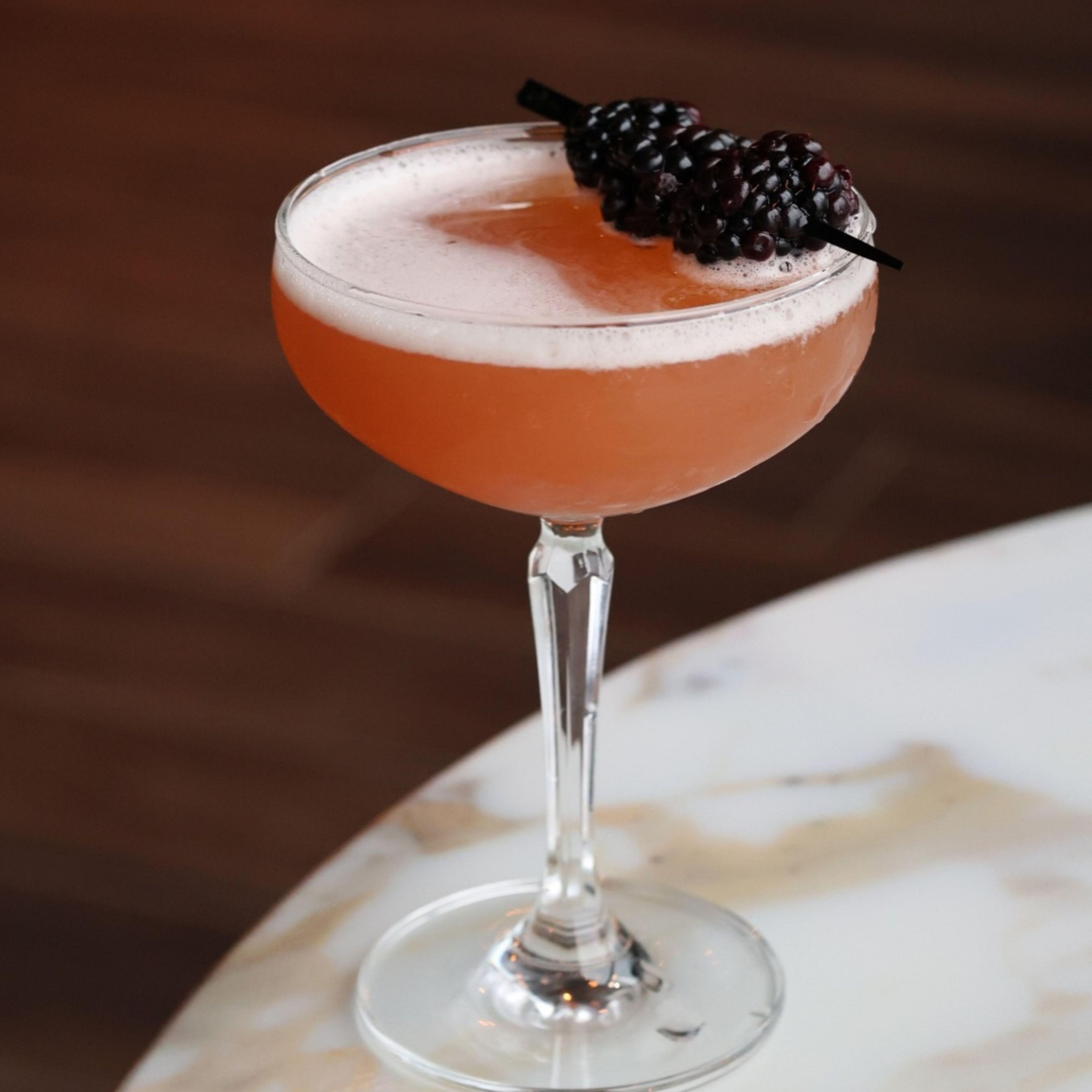 Pink cocktail garnished with a fresh blackberry