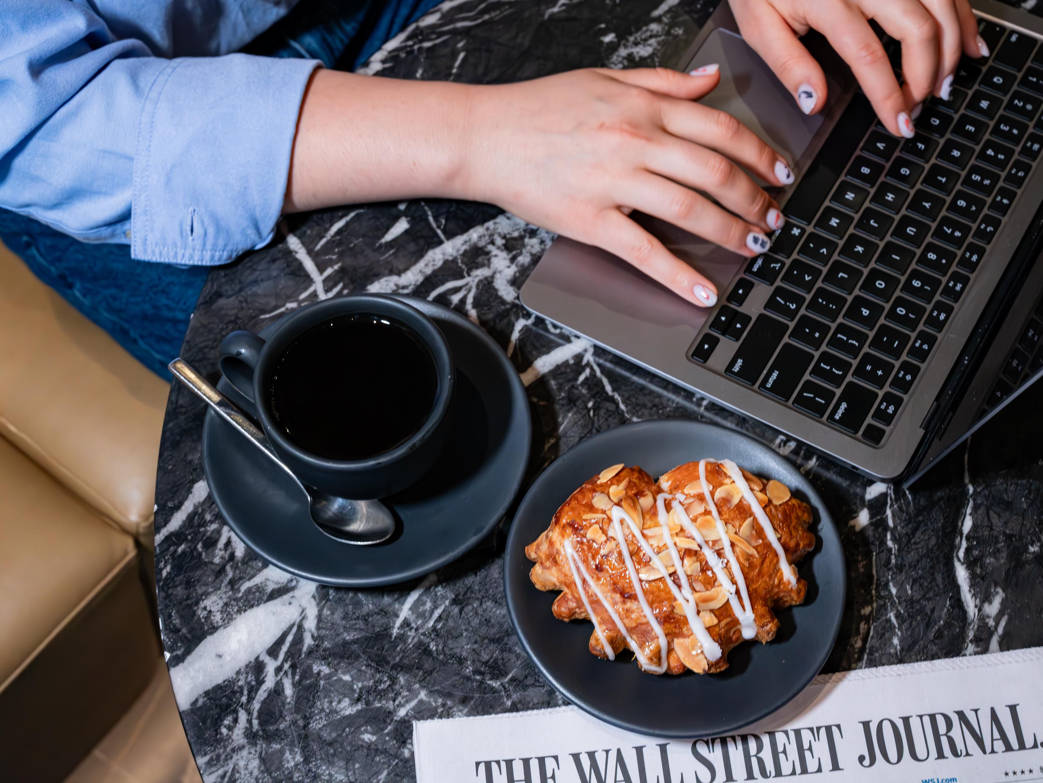 Woman working on laptop in the cafe with coffee and a pastry.