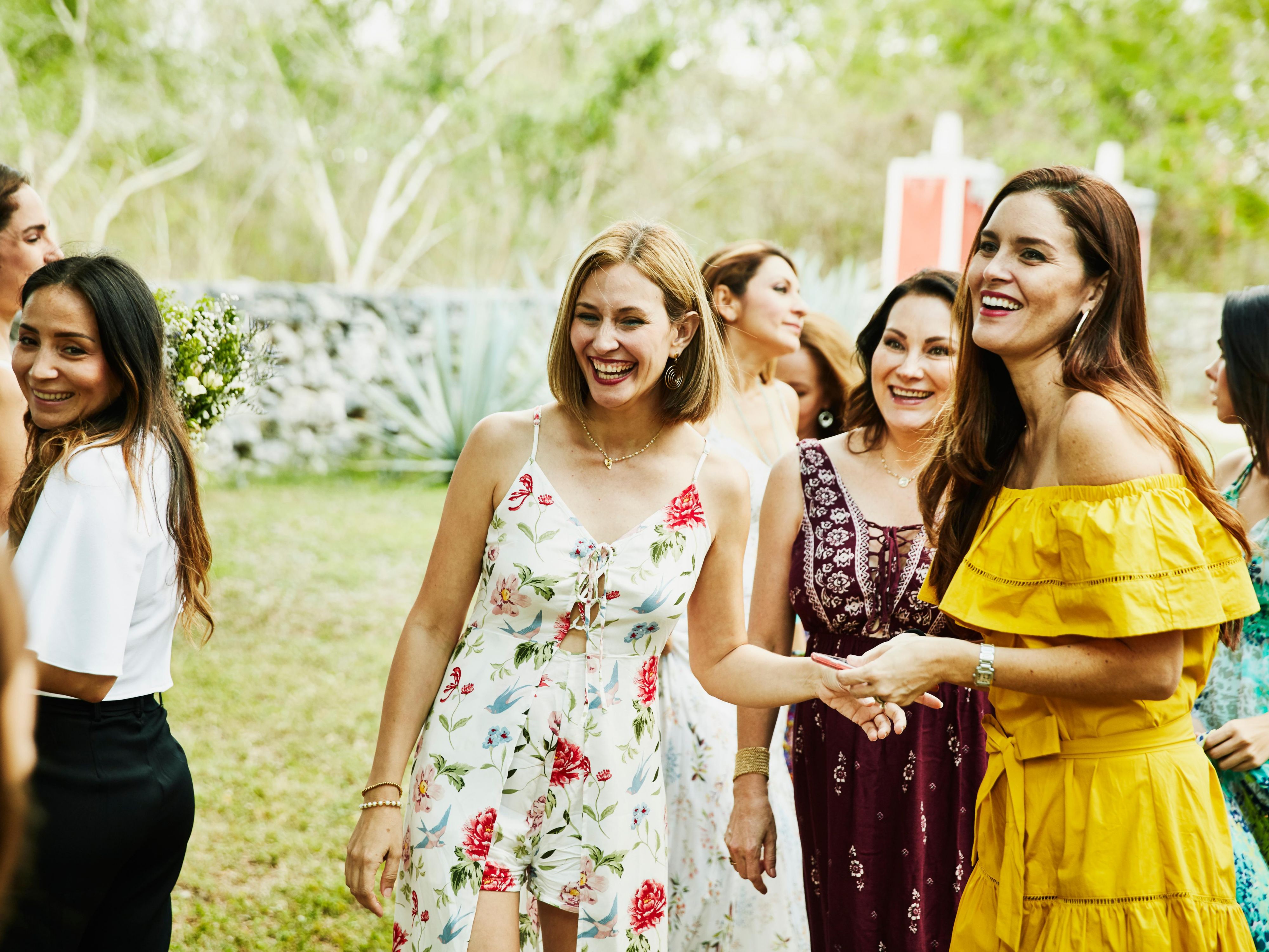 Group of women in colorful dresses smiling and socializing at an outdoor gathering on a sunny day.