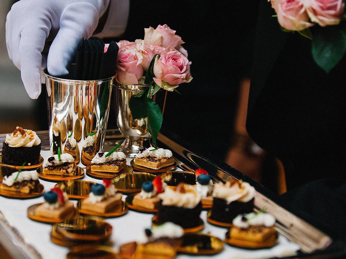 Gloved server arranging bite-sized desserts and hors d’oeuvres on a catering tray.