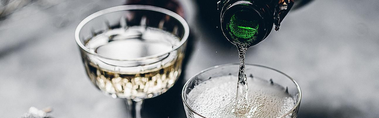Champagne being poured into coupe glasses on a tabletop.