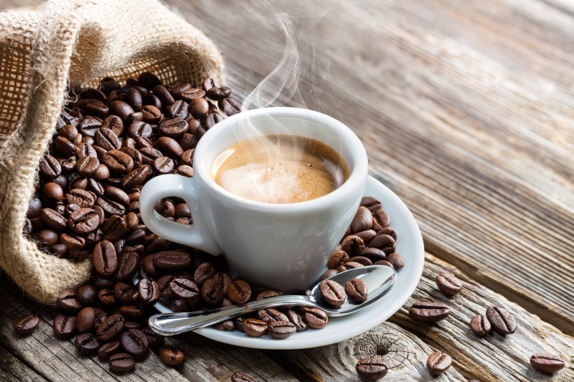 Steaming espresso cup with coffee beans on a rustic wood table
