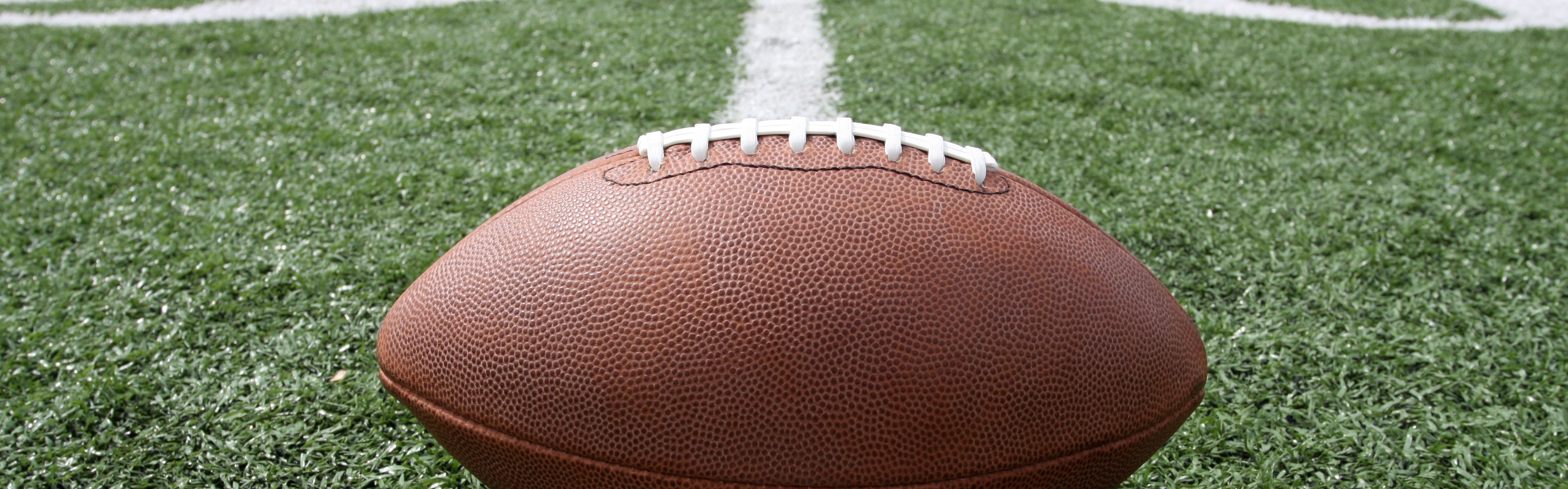 Football resting on a green field with white yard lines