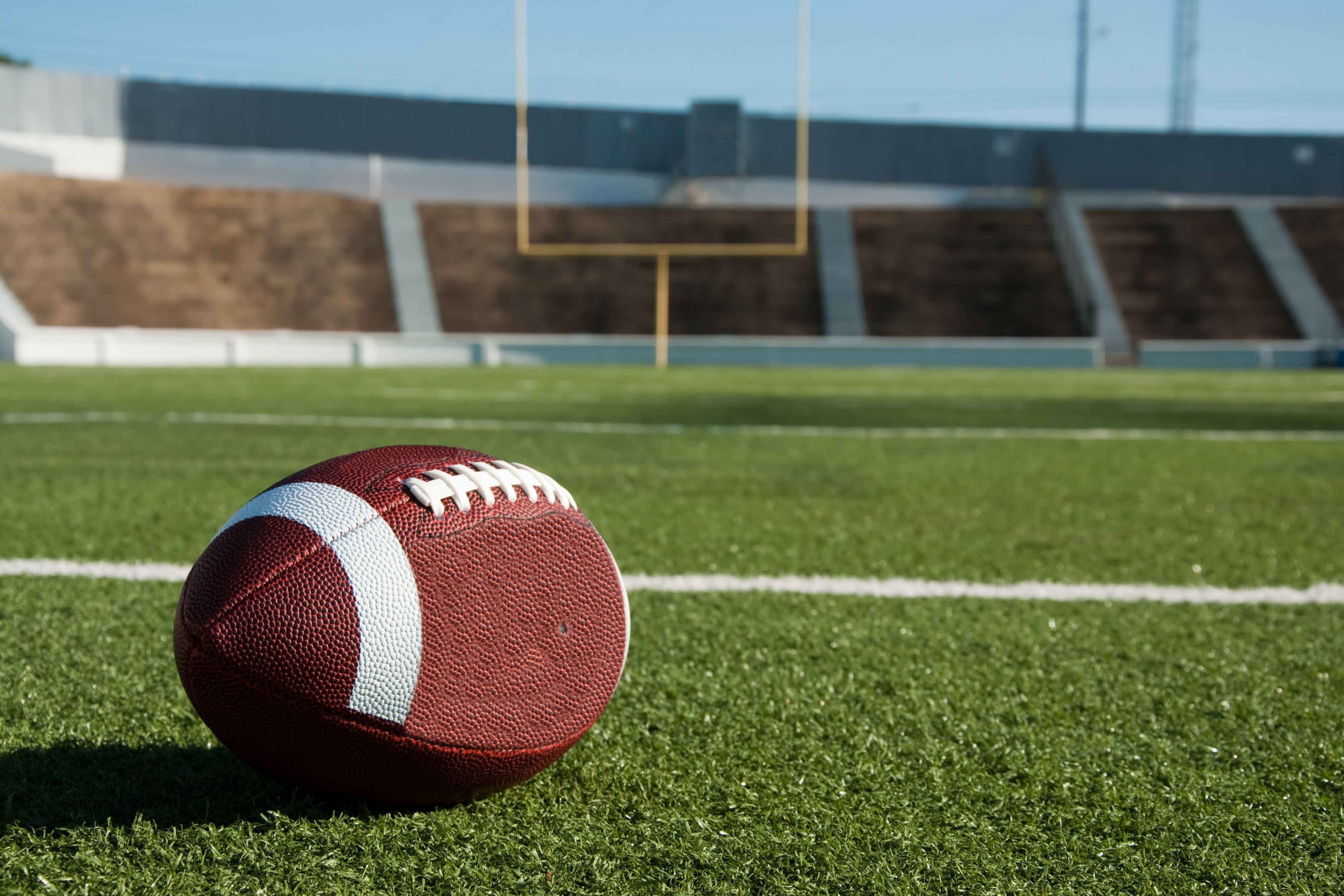 Football resting on a field with goalposts in the distance