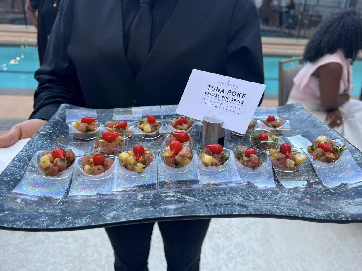 A server holding a tray of food beside a pool. 