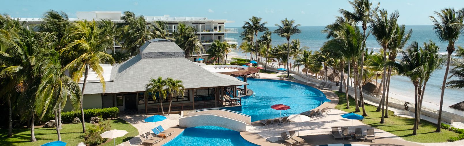Luxury resort pool overlooking beach and palm trees.