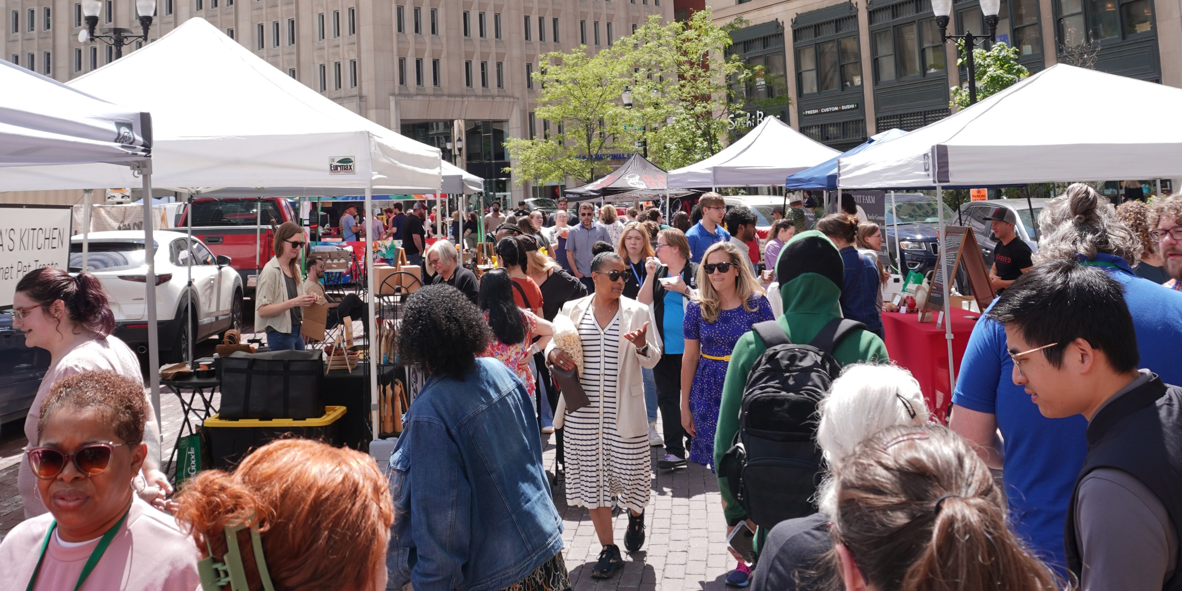 Bustling downtown Indianapolis farmers market with local vendors, white tents, and visitors exploring fresh goods on a sunny day.