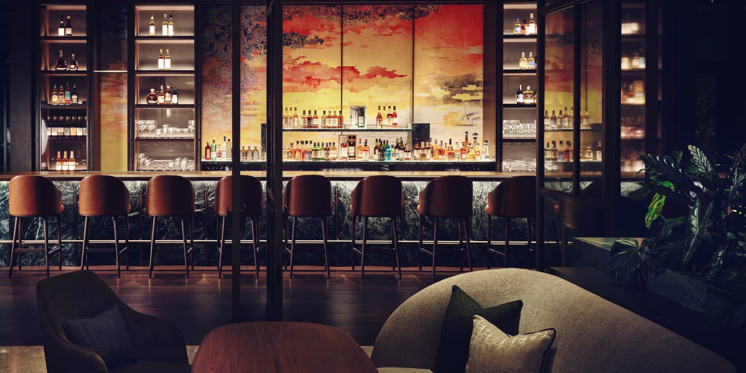 A fully stocked bar with a vibrant mural of reds, oranges, and yellows as a backdrop.